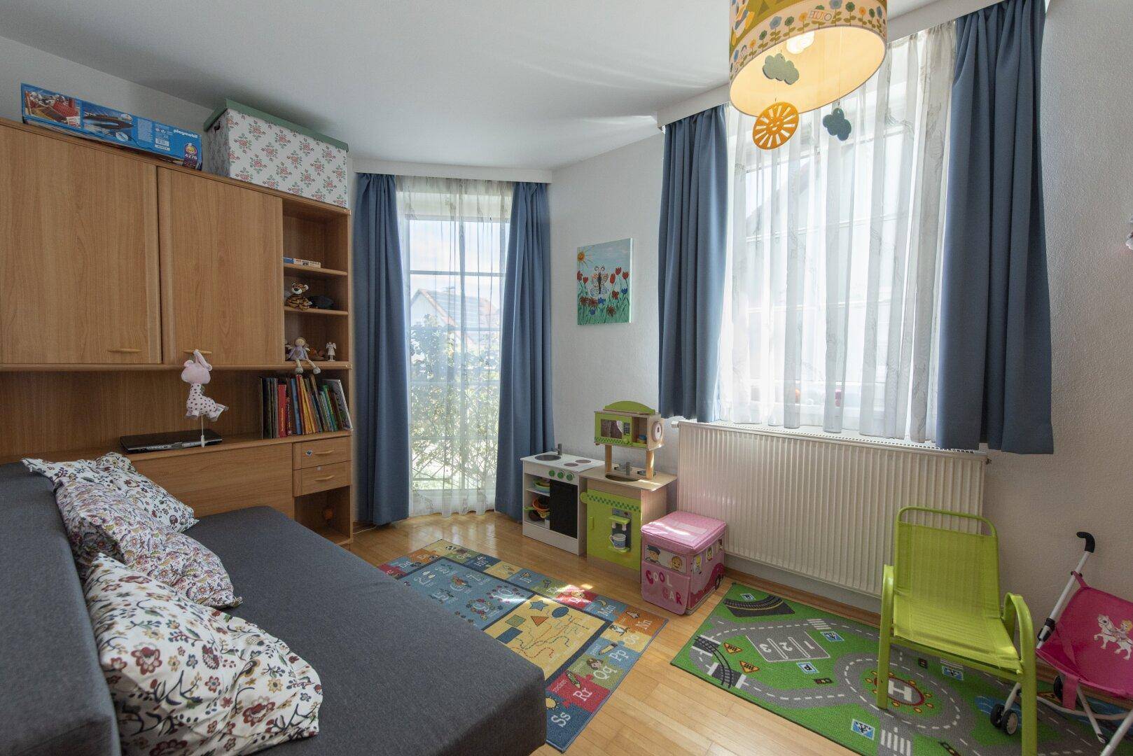 Kinderzimmer mit Holzboden, Spielteppichen und bunten Vorhängen, hell und freundlich.