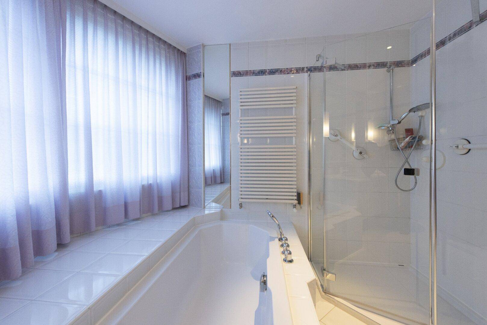 Helles Badezimmer mit Badewanne, Duschkabine und beheiztem Handtuchhalter.
