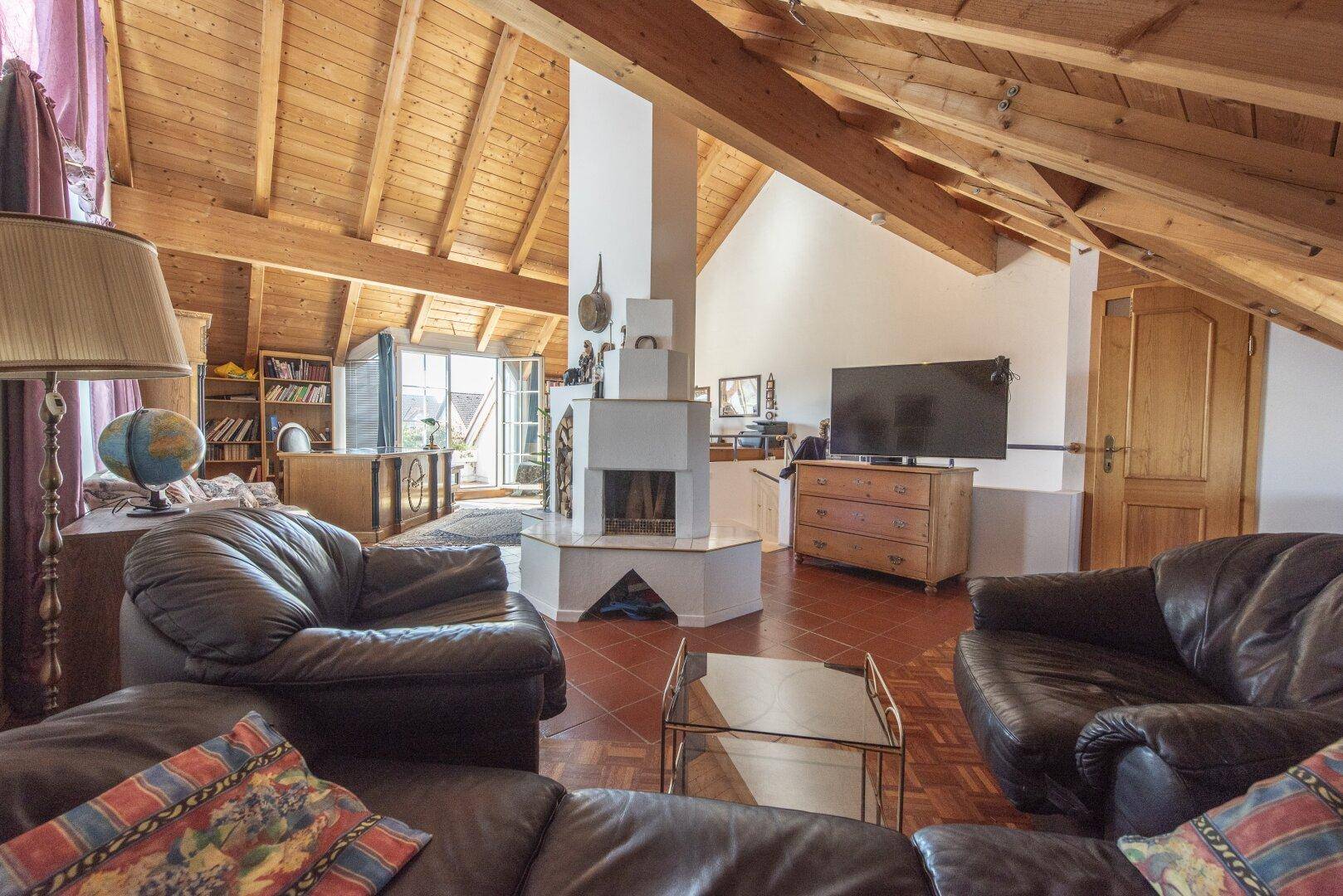 Gemütliches Dachgeschoss-Wohnzimmer mit Holzbalken, Kamin und rustikalem Charme.