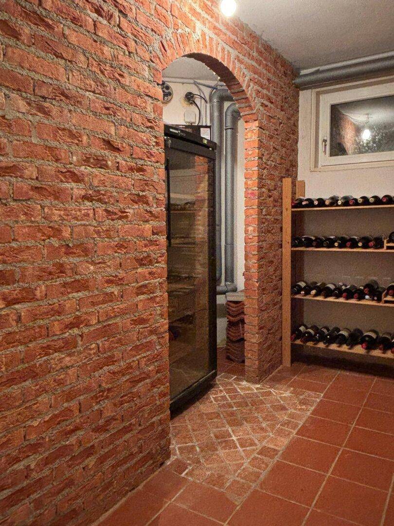 Rustikaler Weinkeller mit Ziegelwänden, Weinregalen und einem Weinkühlschrank.