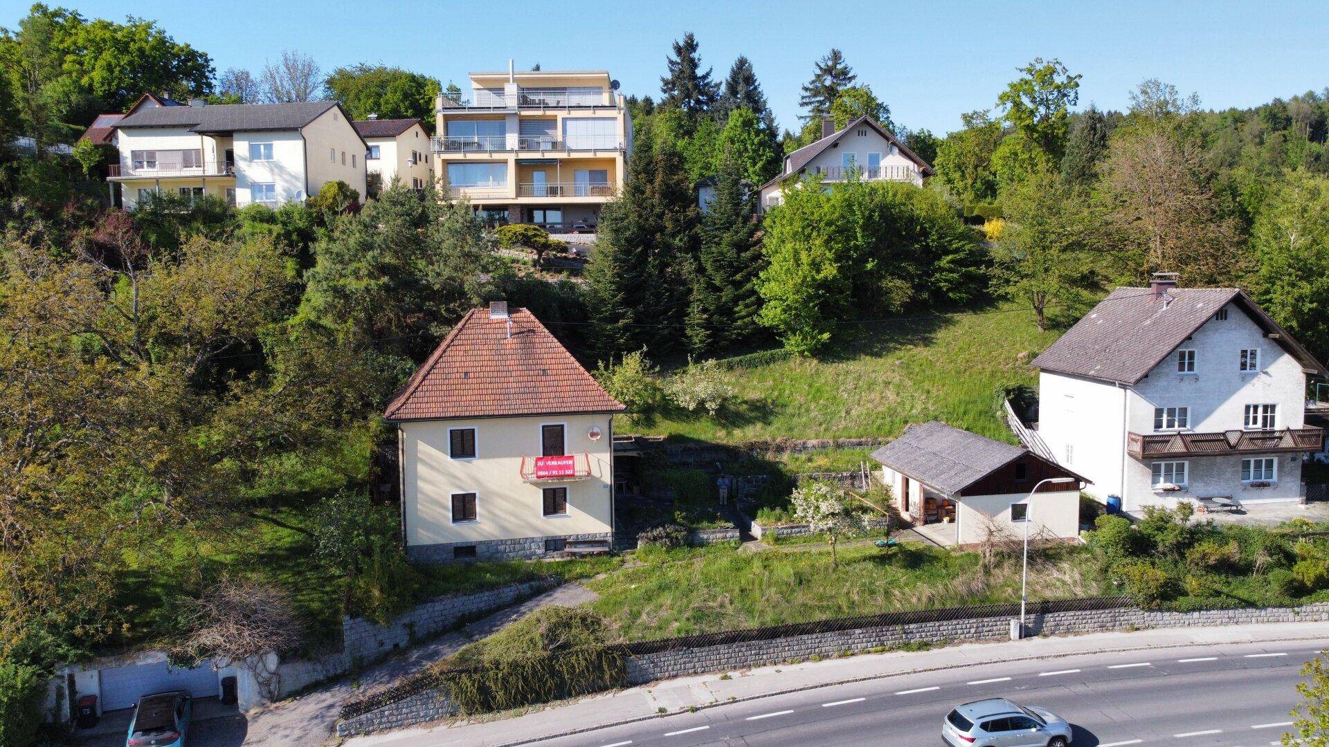 Übersicht des Hauses mit Nebengebäude, umgeben von viel Grün und weiteren Wohnhäusern am Hang.
