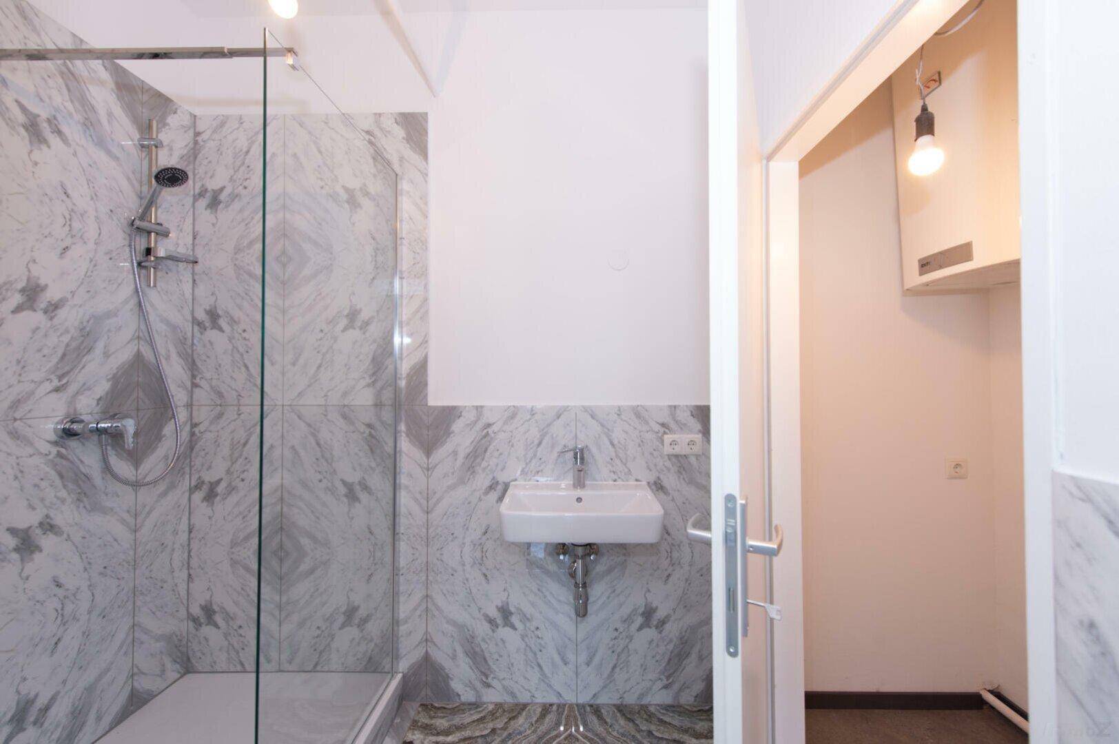 Modernes Badezimmer mit begehbarer Dusche, kleinem Waschbecken und eleganten Marmorfliesen.