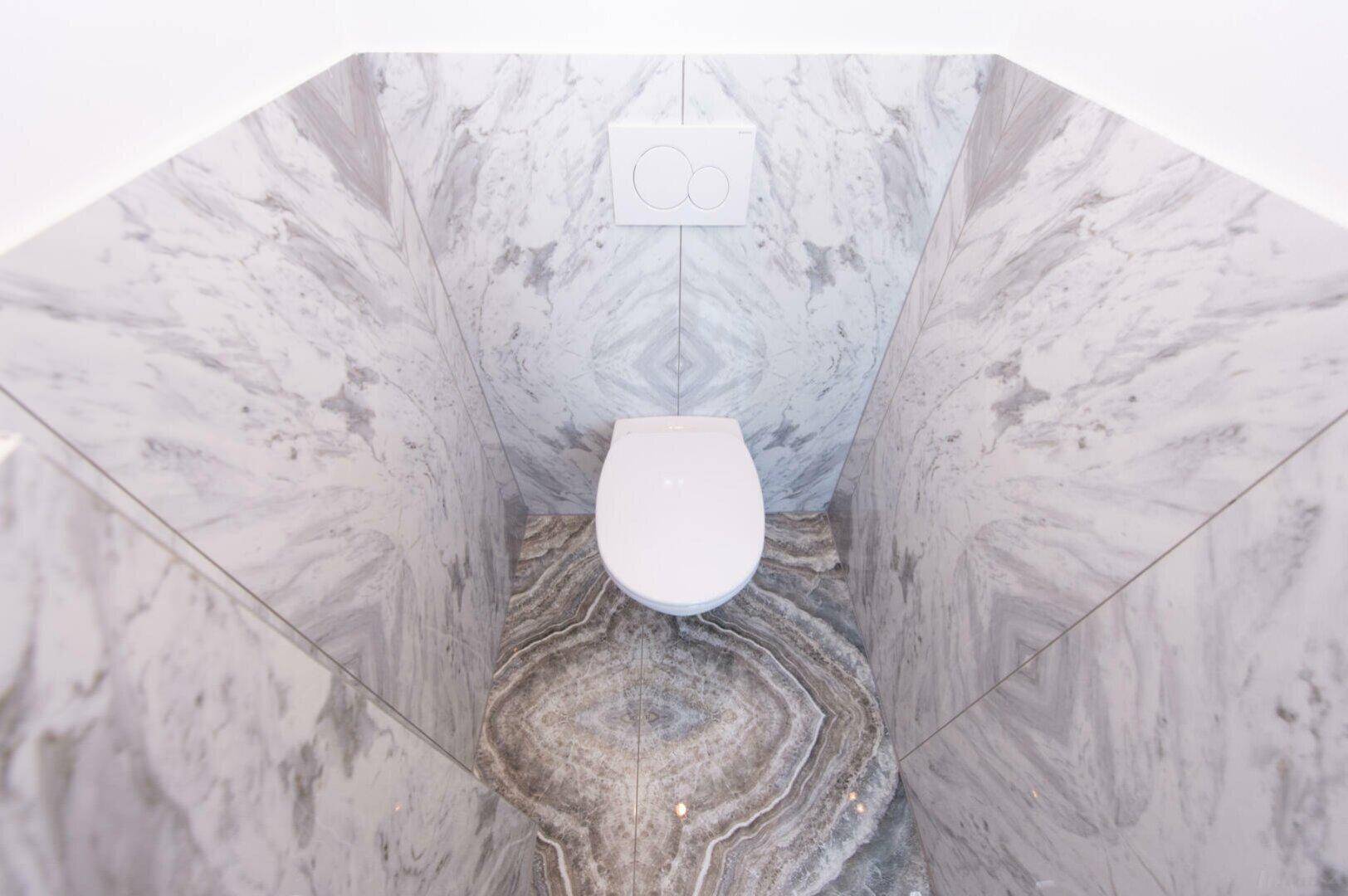 Kleines WC mit wandhängender Toilette und auffälligen Marmorfliesen an Wänden und Boden.