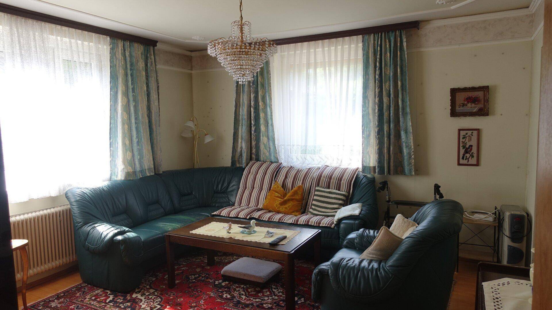 Wohnzimmer mit Ledersofa, Kronleuchter und traditionellem Teppichboden.
