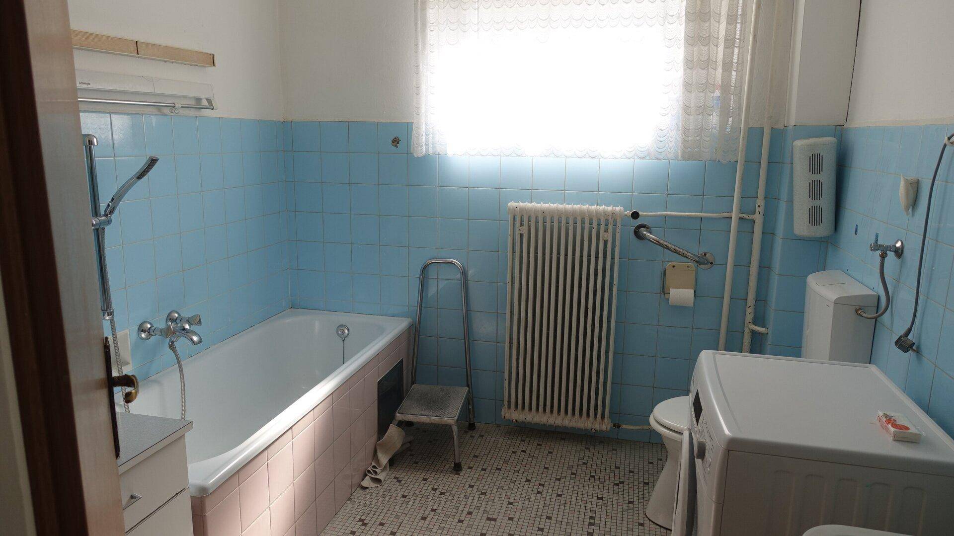Badezimmer im Stil der 80er Jahre mit blauen Fliesen, Badewanne und Fenster.