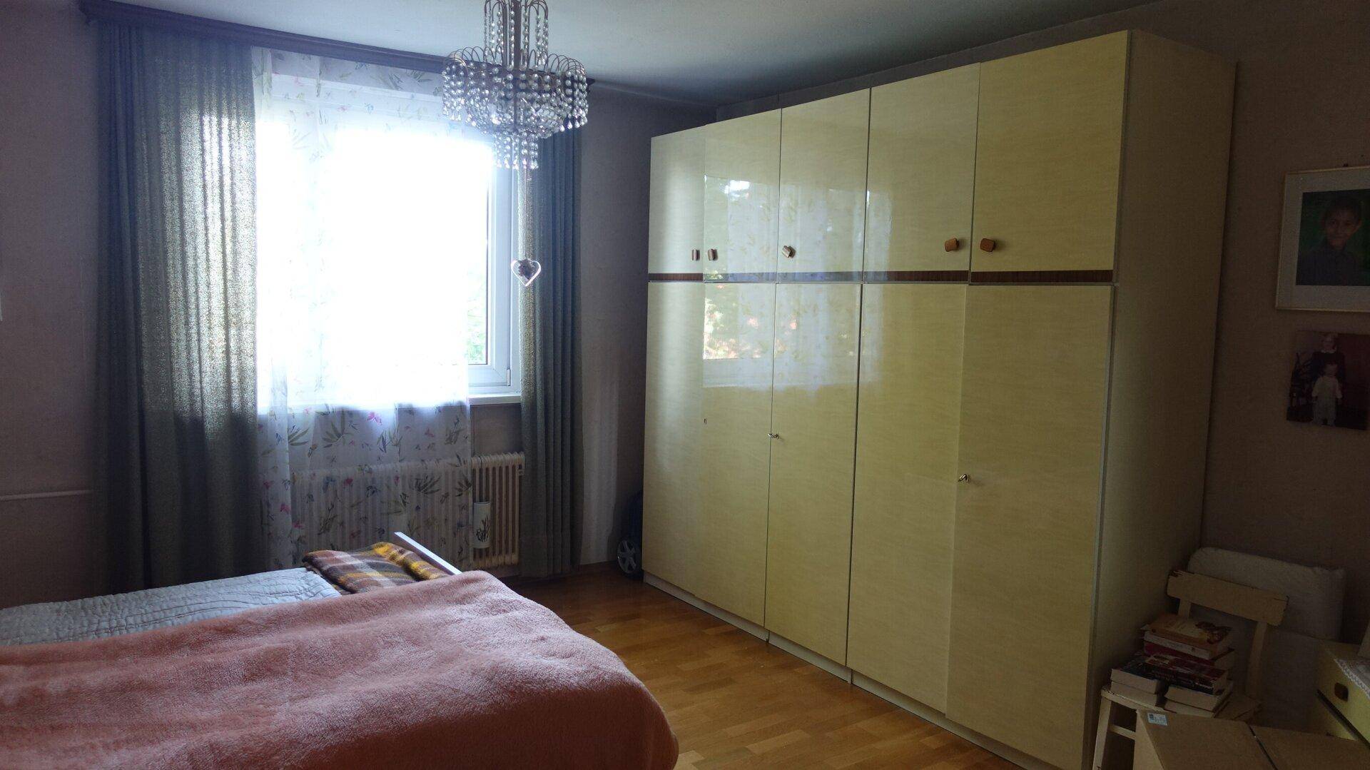 Schlafzimmer mit großem Kleiderschrank, Holzboden und viel Tageslicht durch das Fenster.