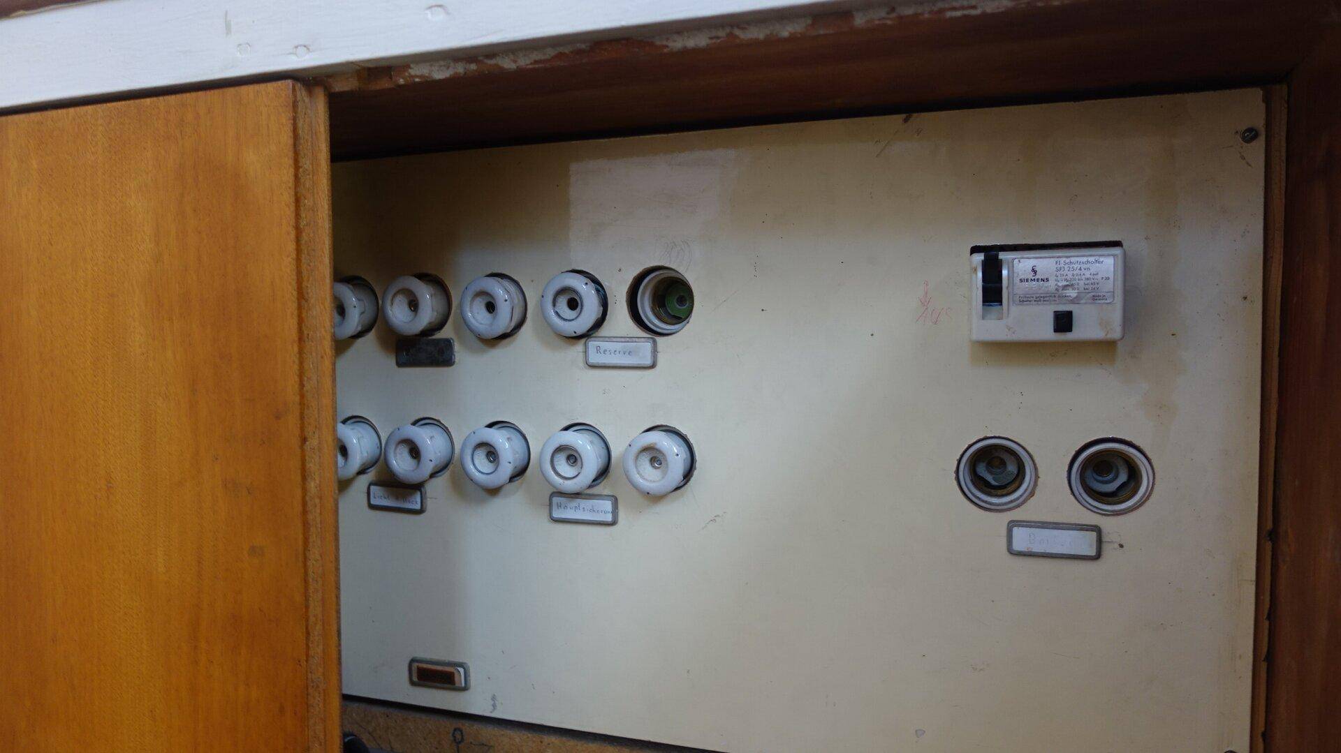 Alter Sicherungskasten mit Keramiksicherungen in einem Hauswirtschaftsraum.