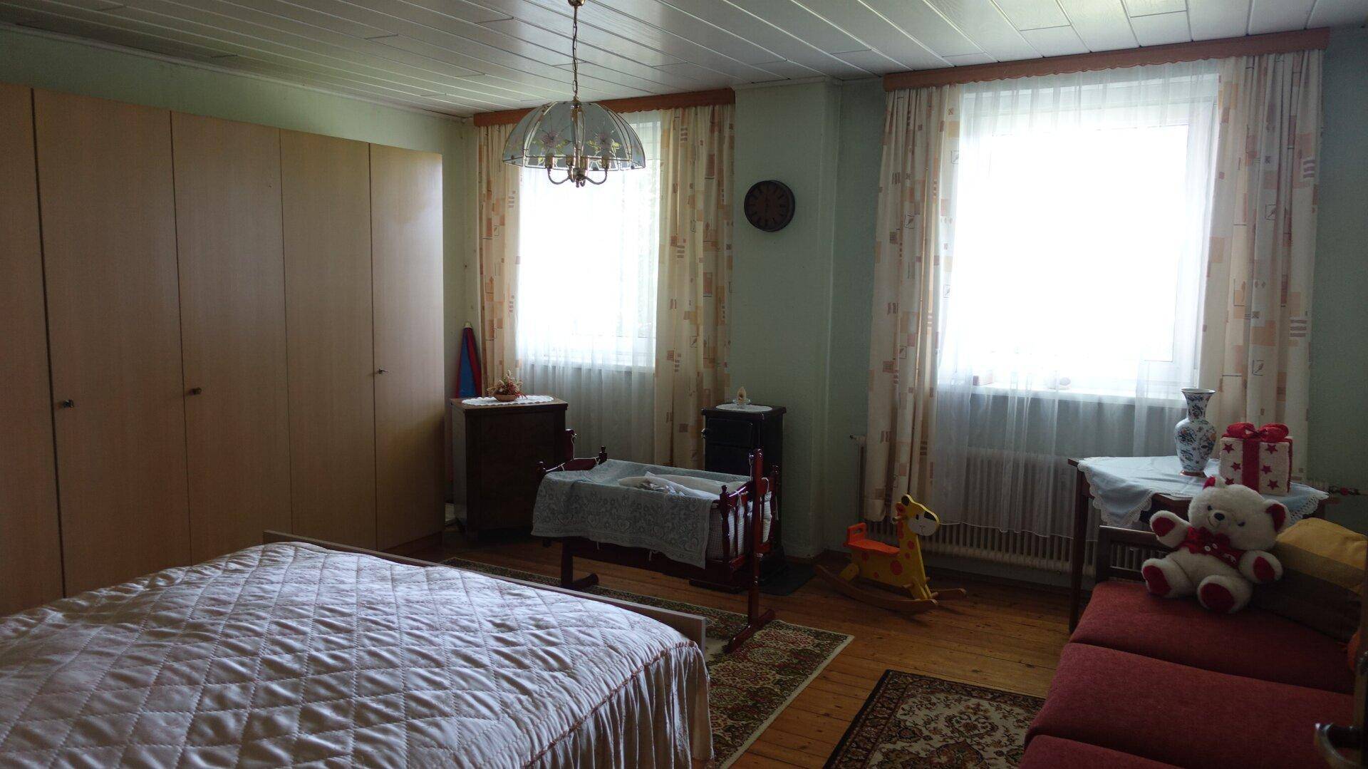 Schlafzimmer mit zwei Fenstern, Holzboden und großem Kleiderschrank, hell und geräumig.