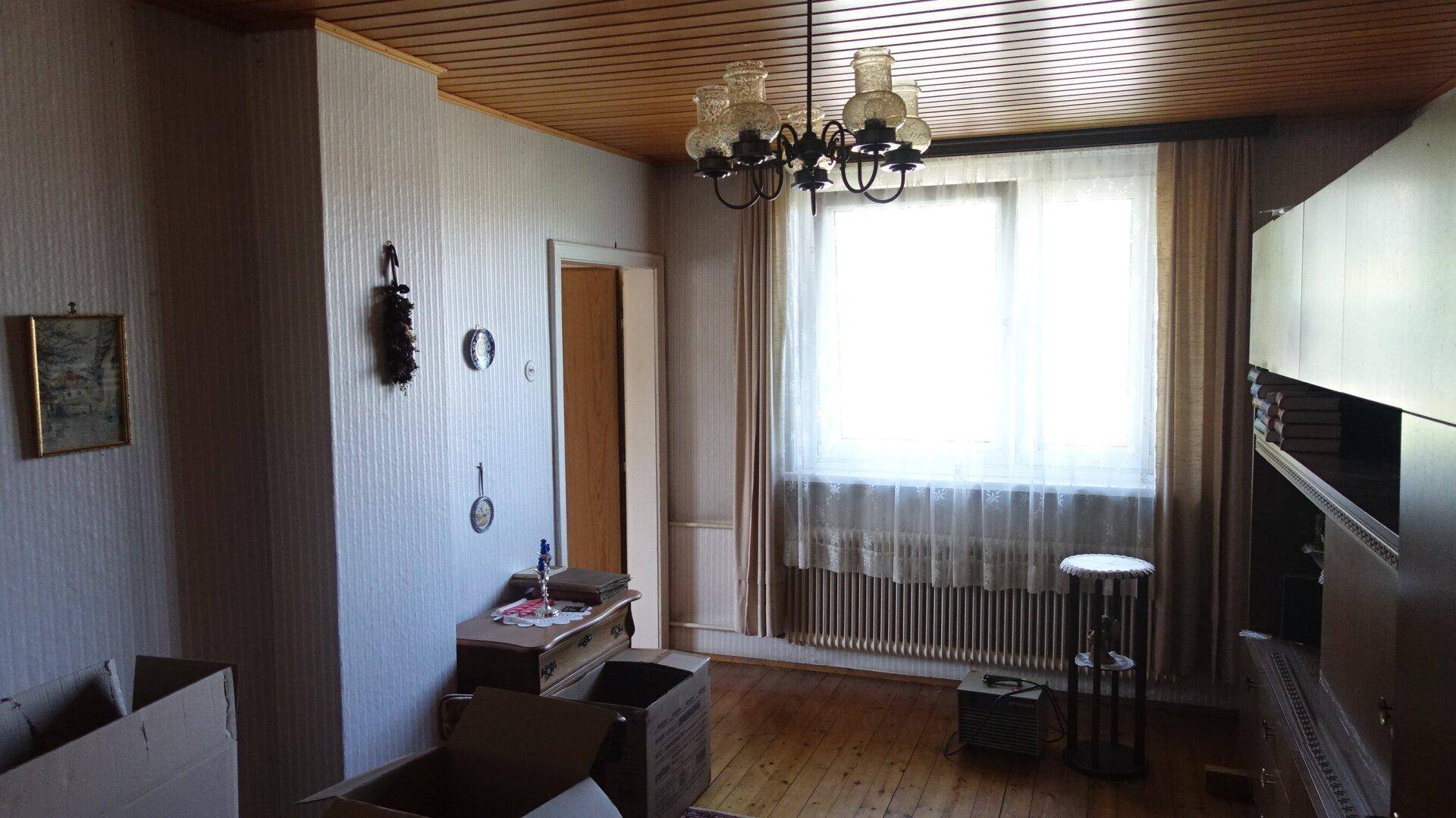 Wohnzimmer mit Holzboden, großem Fenster und traditioneller Einrichtung, teilweise mit Umzugskartons.