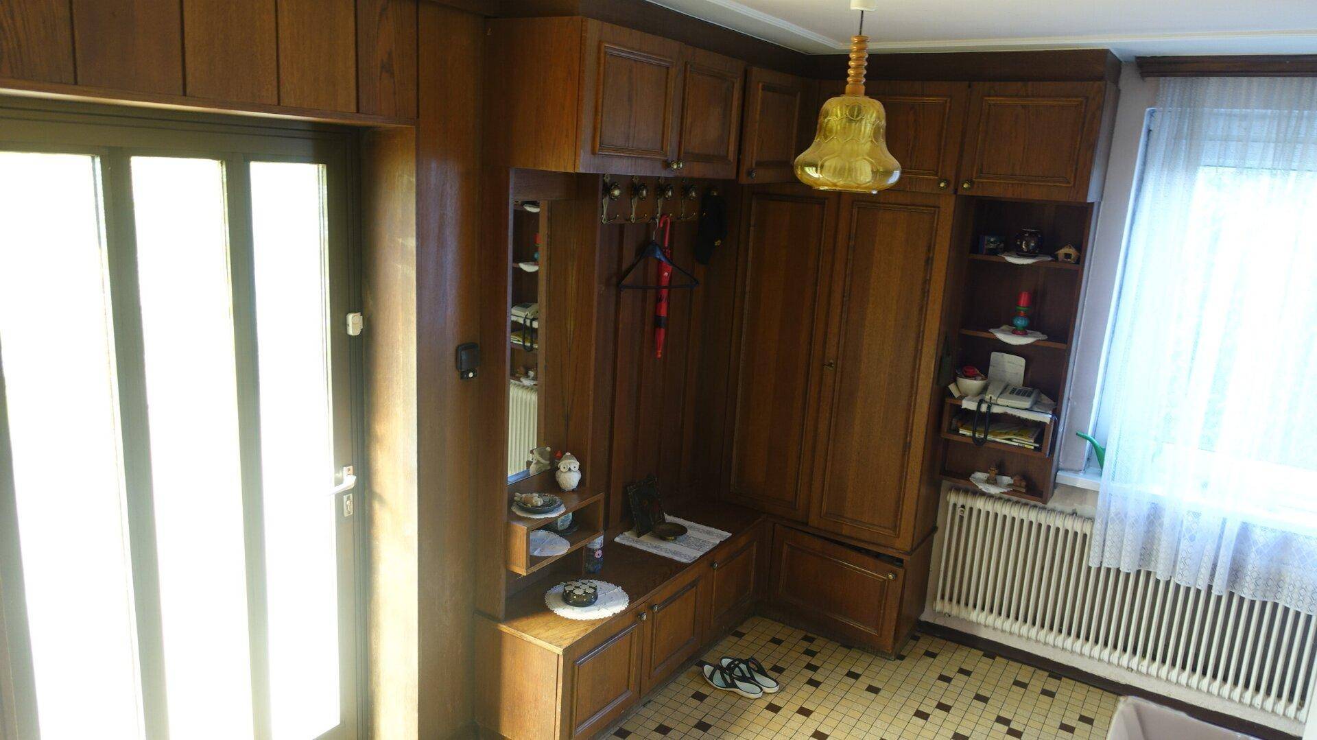 Eingangsbereich mit Holzvertäfelung, Garderobe und Fliesenboden, hell durch das Fenster.