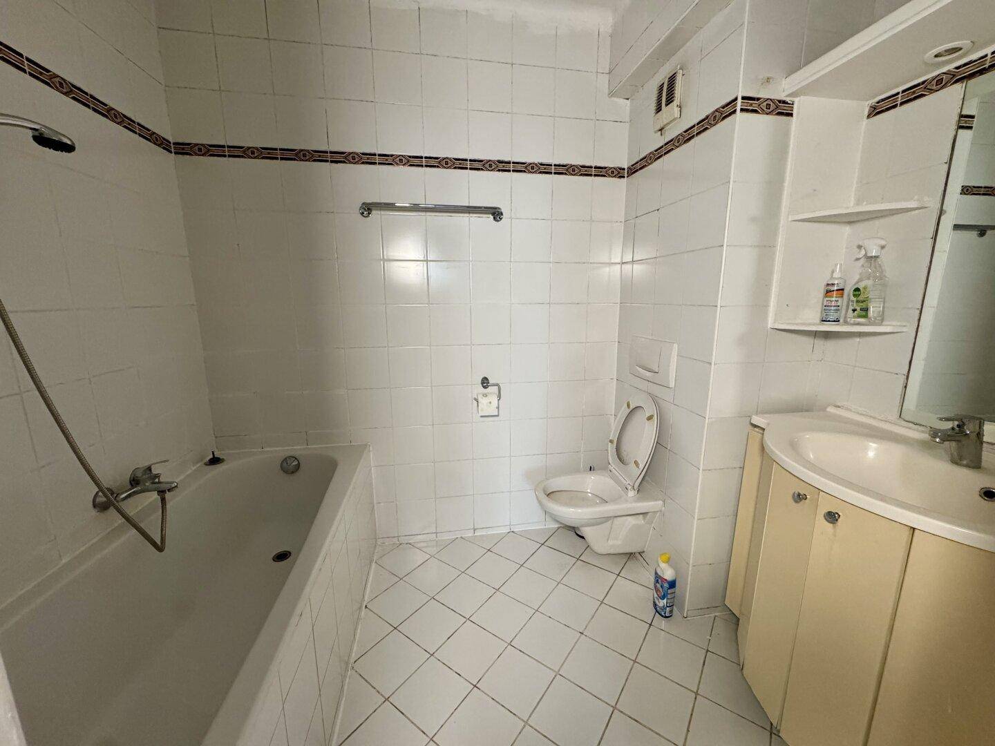 Gefliestes Badezimmer mit Badewanne, Toilette und Waschbeckenunterschrank im 80er-Jahre-Stil.