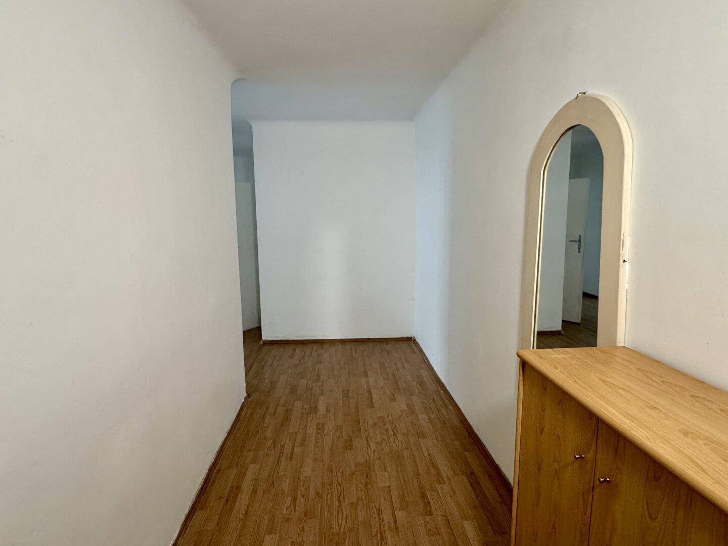 Langer Flur mit Laminatboden und einem dekorativen Spiegelbogen.