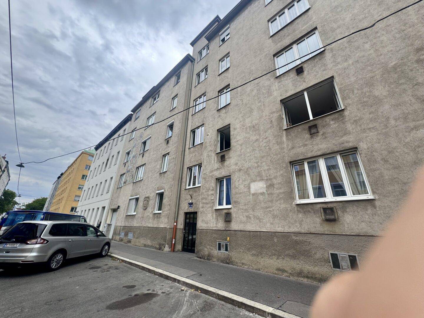 Fassade eines Mehrfamilienhauses an einer städtischen Straße mit parkendem Auto.