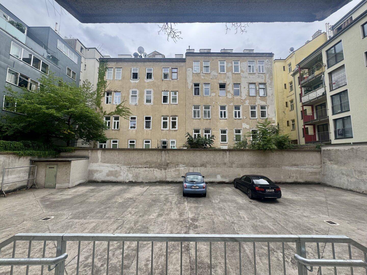 Hinterhof-Parkplatz mit zwei Autos und Blick auf die Rückseite des Gebäudes.