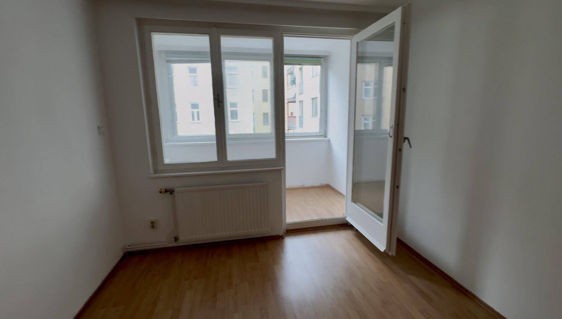 Helles Zimmer mit Laminatboden und Zugang zu einem verglasten Balkon.