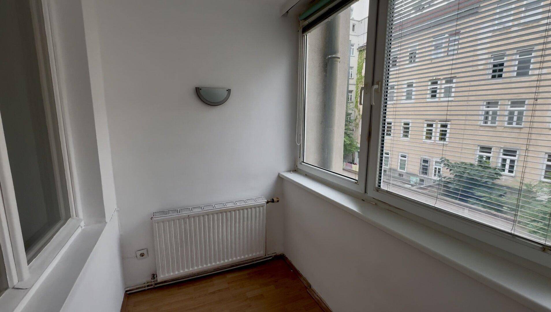 Heller, verglaster Balkon mit Heizung und Blick auf die gegenüberliegenden Gebäude.