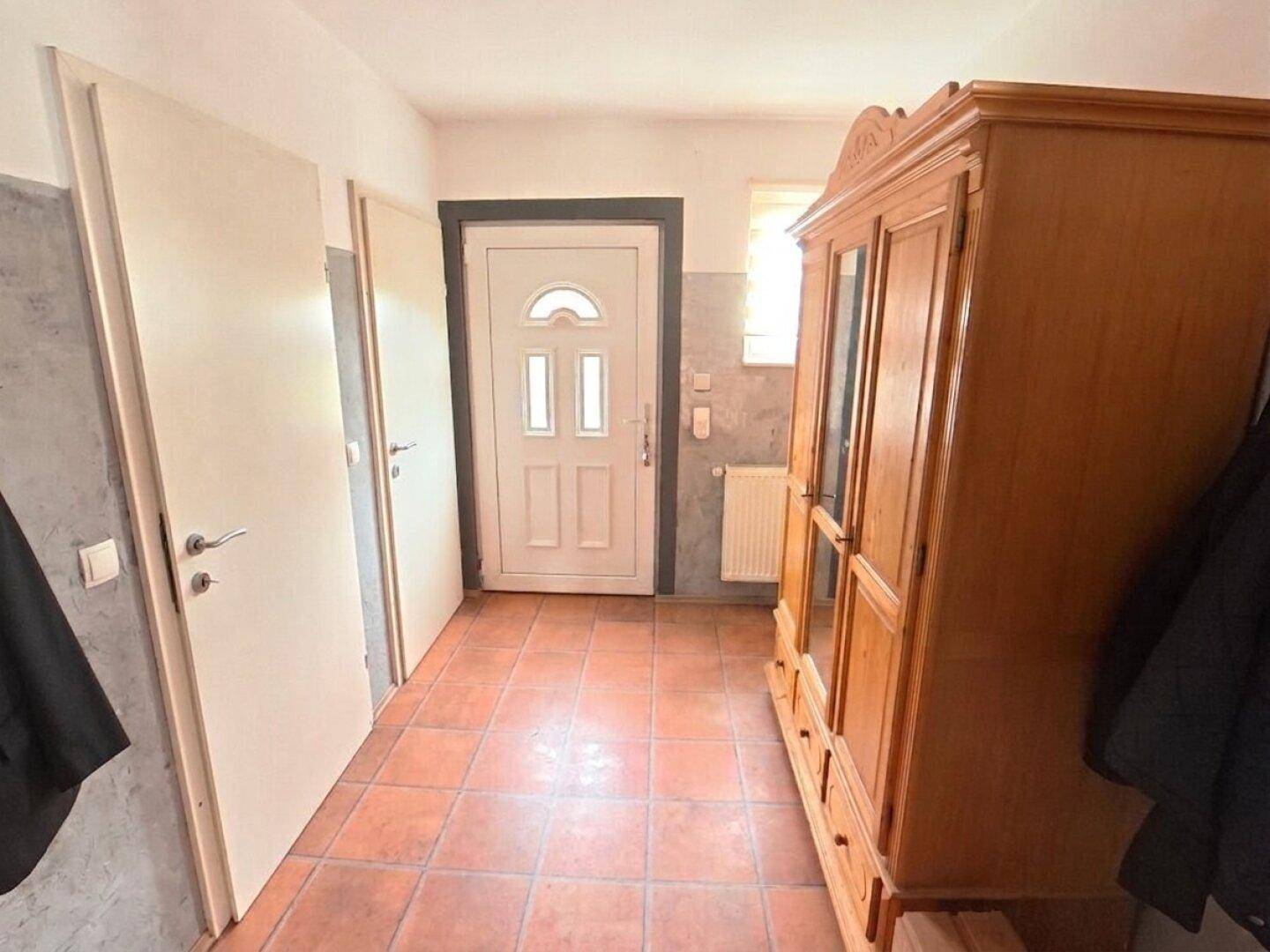 Eingangsbereich mit Terrakotta-Fliesenboden und einem traditionellen Holzschrank.