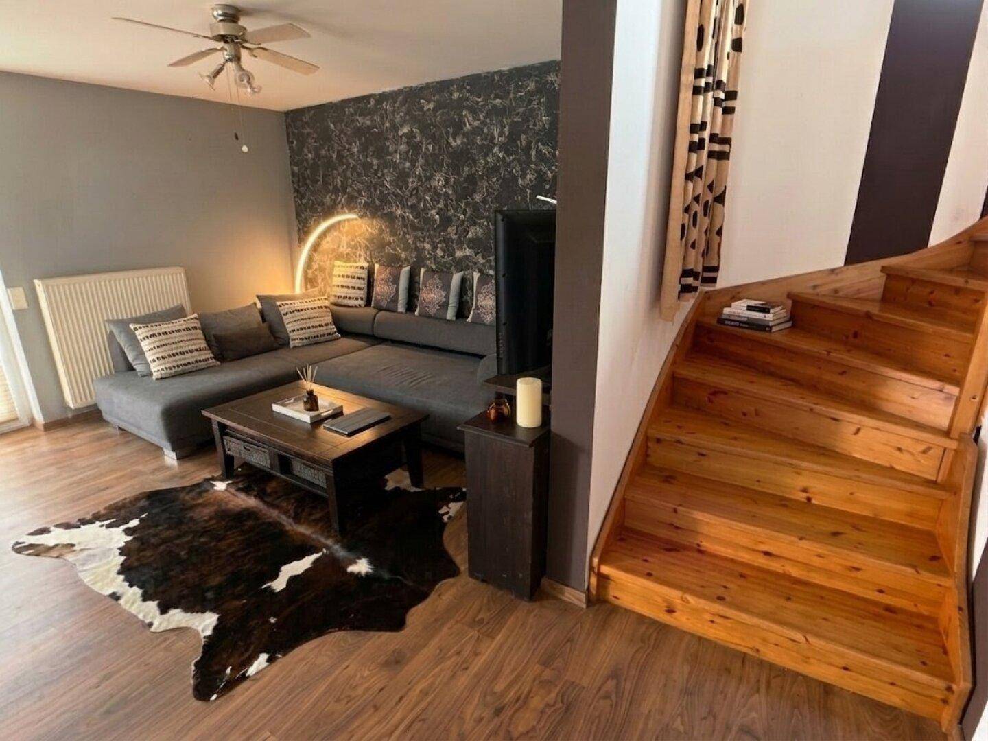 Gemütliches Wohnzimmer mit Sofa, Couchtisch und Holztreppe zum Obergeschoss.