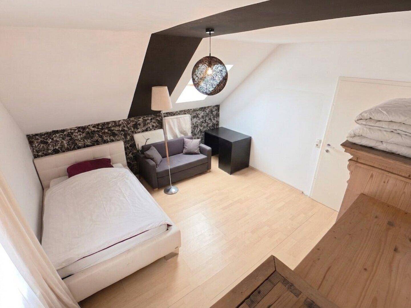 Schlafzimmer mit Einzelbett, Sofa, Schreibtisch und Dachschräge.