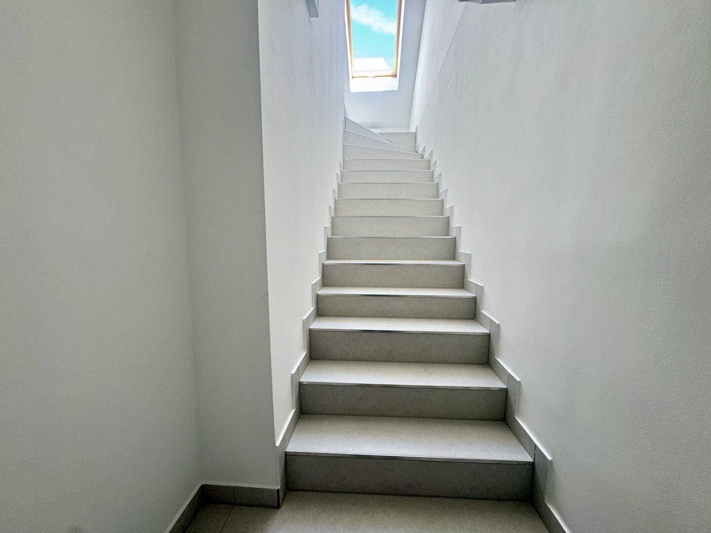 Helles Treppenhaus mit weißen Wänden und einem Oberlicht, das viel natürliches Licht hereinlässt.