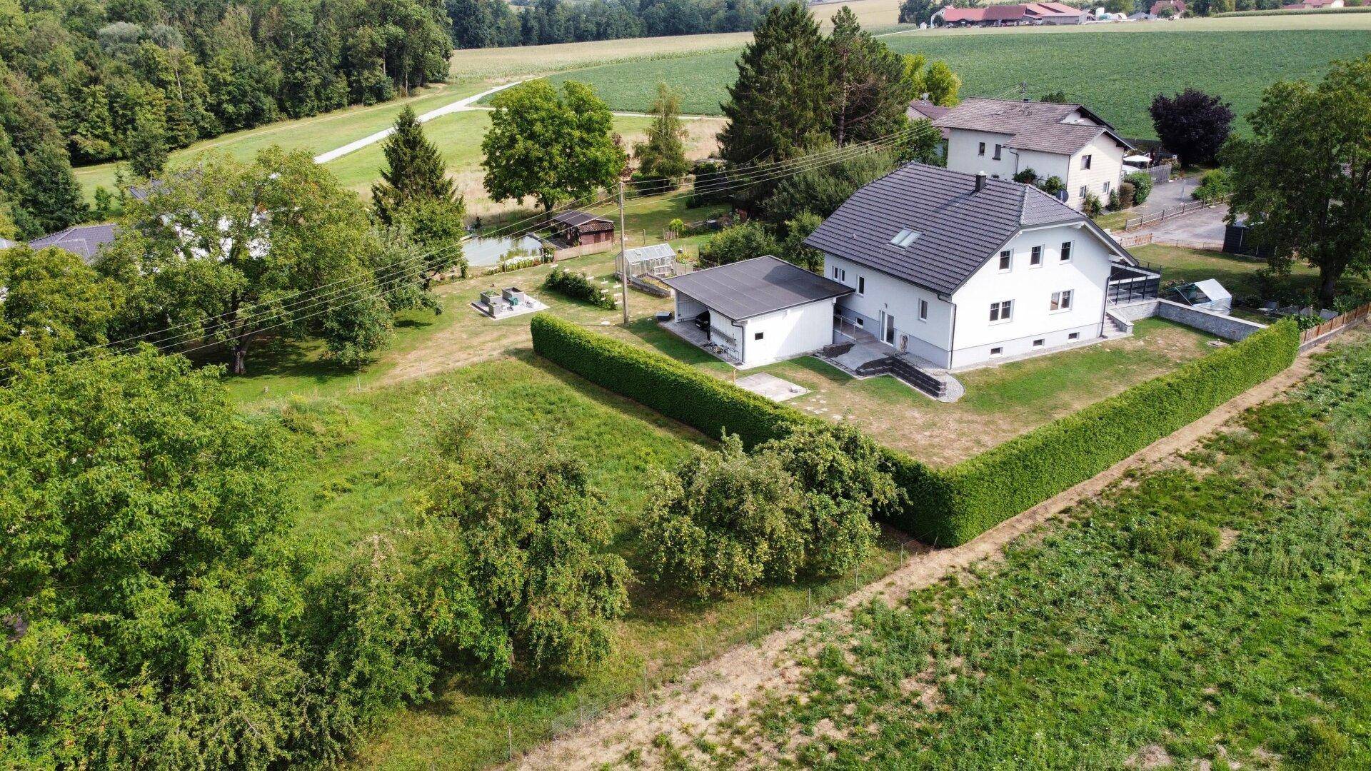 Weitläufige Luftaufnahme des Hauses mit angrenzendem Carport und umgebender grüner Landschaft.