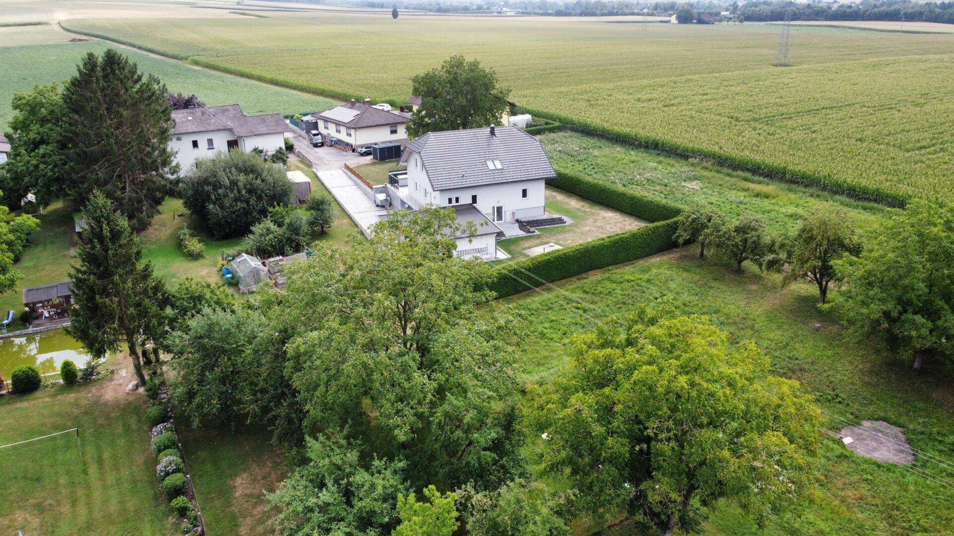 Panoramablick auf das Wohnhaus, umgeben von Feldern und weiteren Häusern in ländlicher Umgebung.