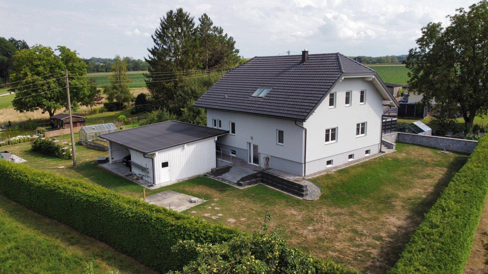 Rückansicht des Hauses mit Carport und Gartenbereich, eingebettet in eine grüne Landschaft.