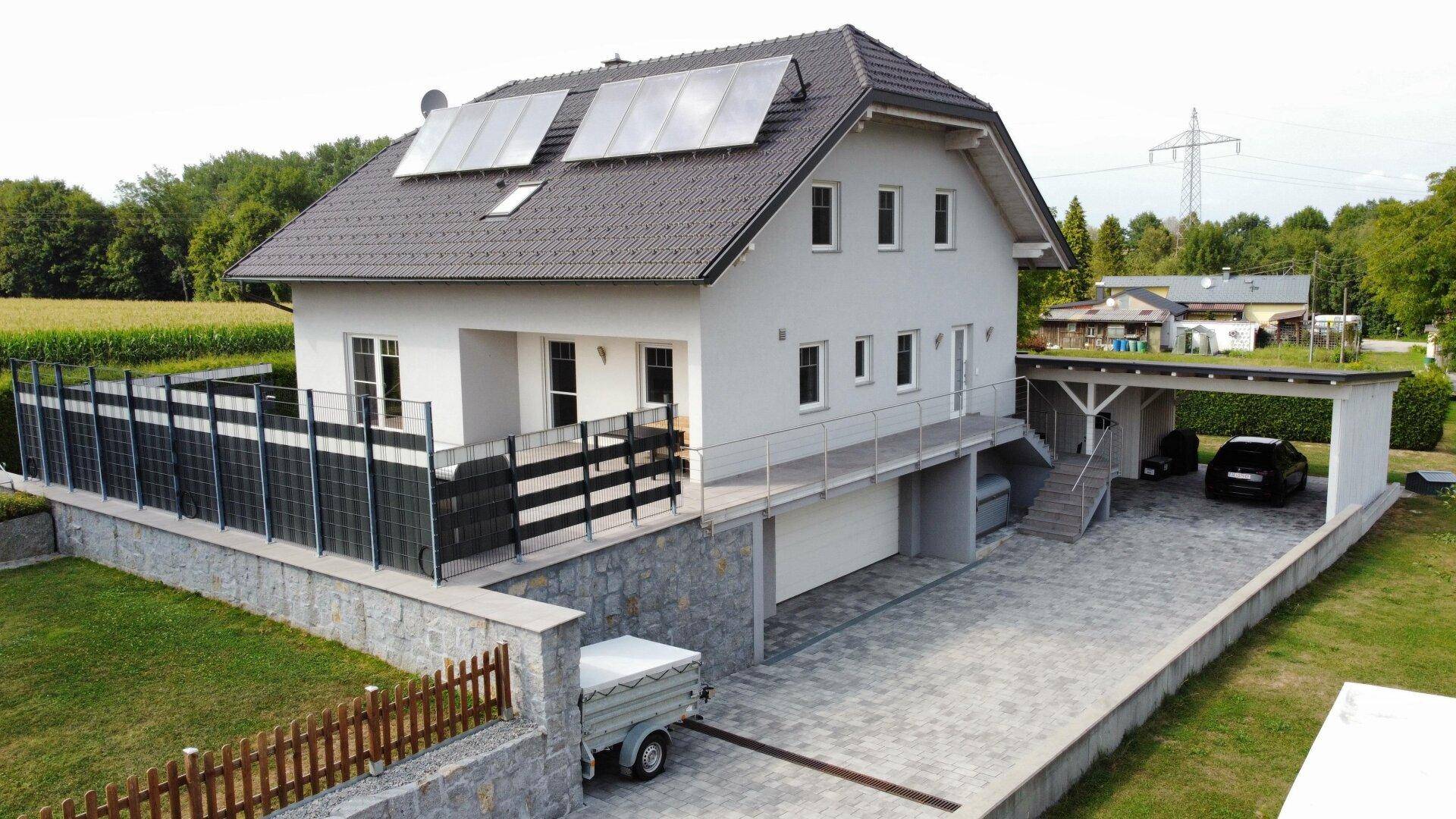 Ansicht des Hauses mit integrierter Garage, Carport und gepflasterter Zufahrt.