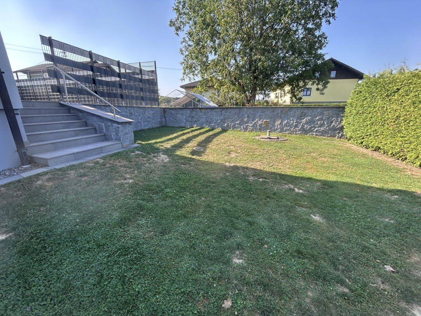 Kleiner Gartenbereich neben der Treppe mit Rasenfläche und Steinmauer.