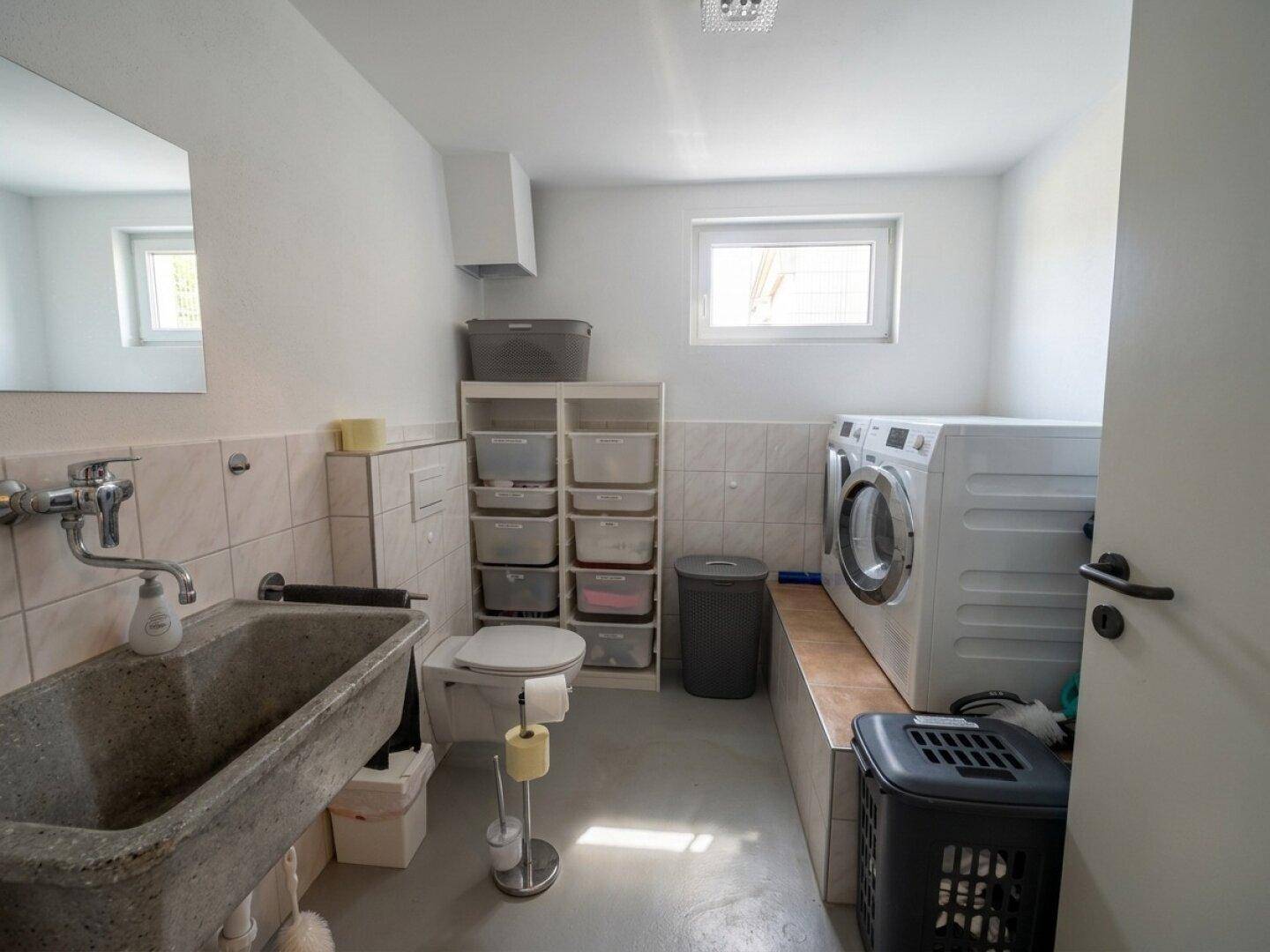 Waschküche mit Waschmaschine, Trockner, Waschbecken und Fenster für natürliche Belüftung.