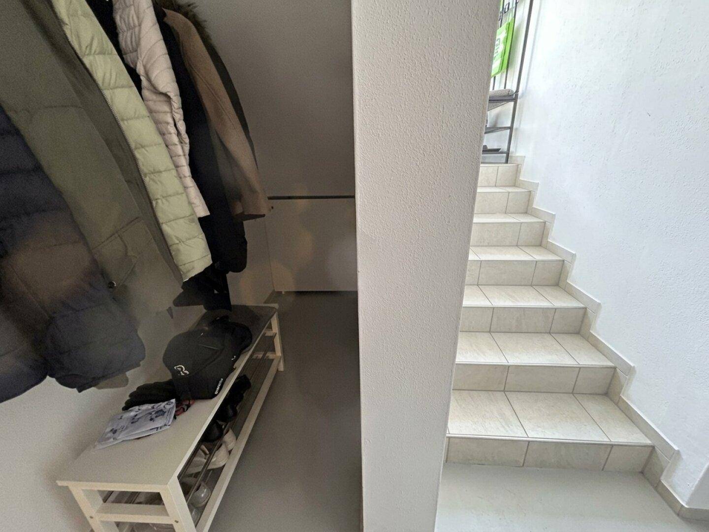 Heller Flur mit gefliester Treppe und Garderobenbereich für Jacken und Schuhe.