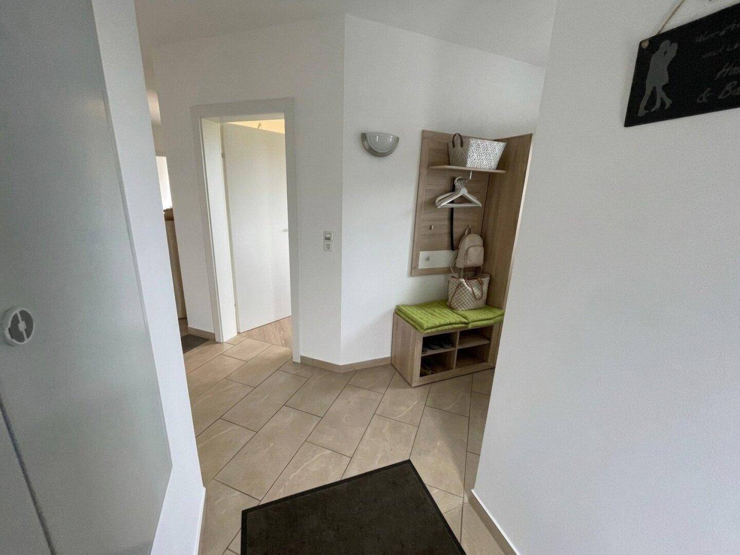 Eingangsbereich mit Garderobe, Schuhbank und hellem Fliesenboden.