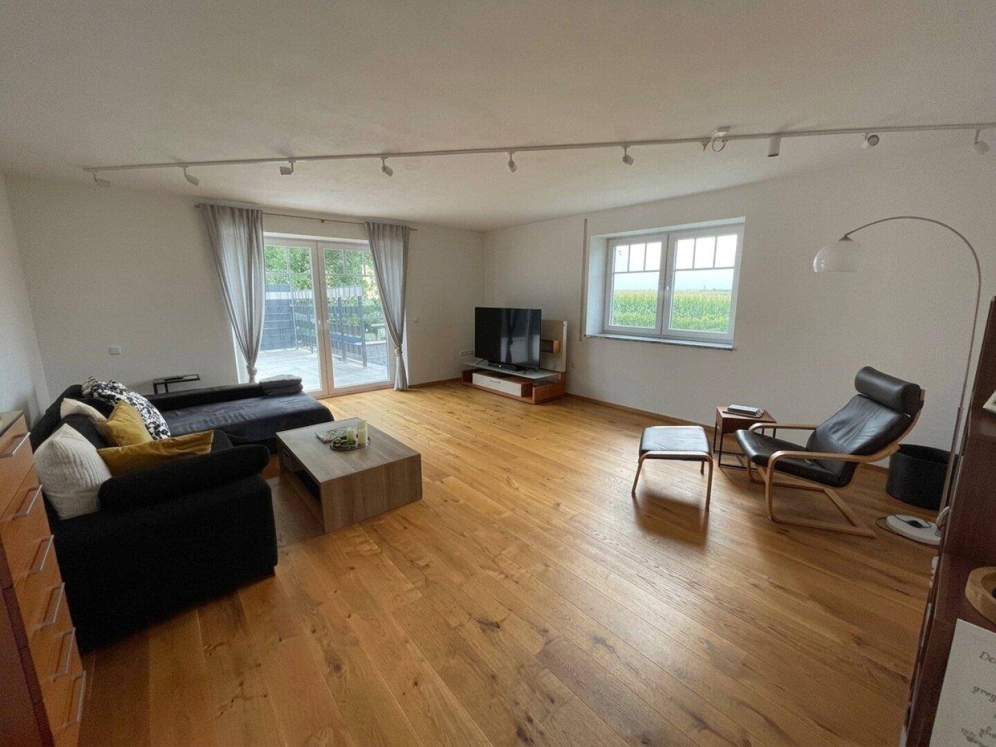 Geräumiges Wohnzimmer mit hellem Holzboden, großen Fenstern und Zugang zur Terrasse.