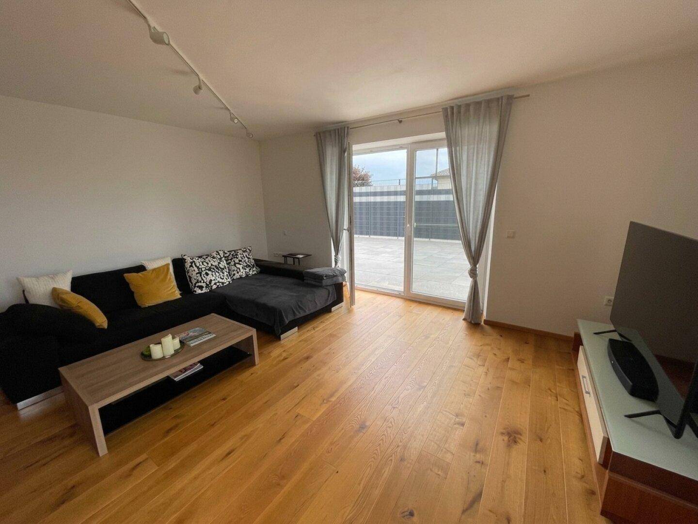 Helles Wohnzimmer mit Holzboden, schwarzem Sofa und Zugang zur Terrasse.