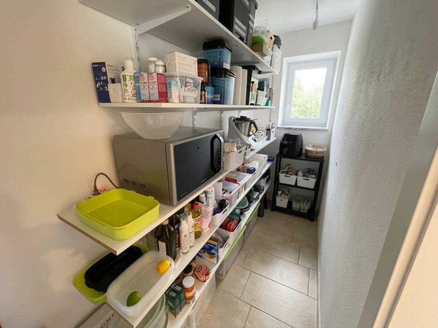 Praktische Speisekammer mit Regalen, Mikrowelle und Fenster für Tageslicht.