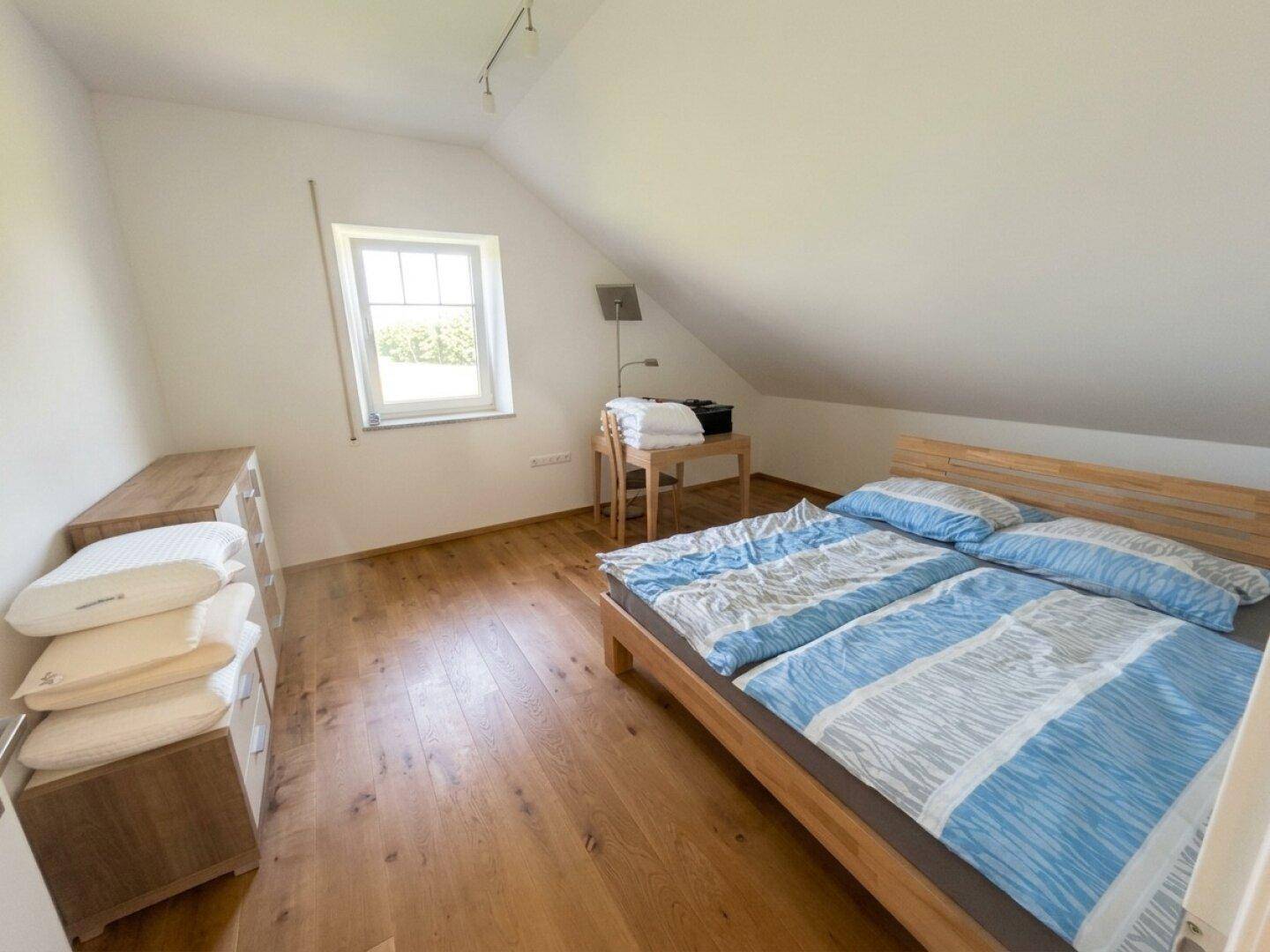 Helles Schlafzimmer mit Holzboden, Fenster und einfacher Einrichtung.