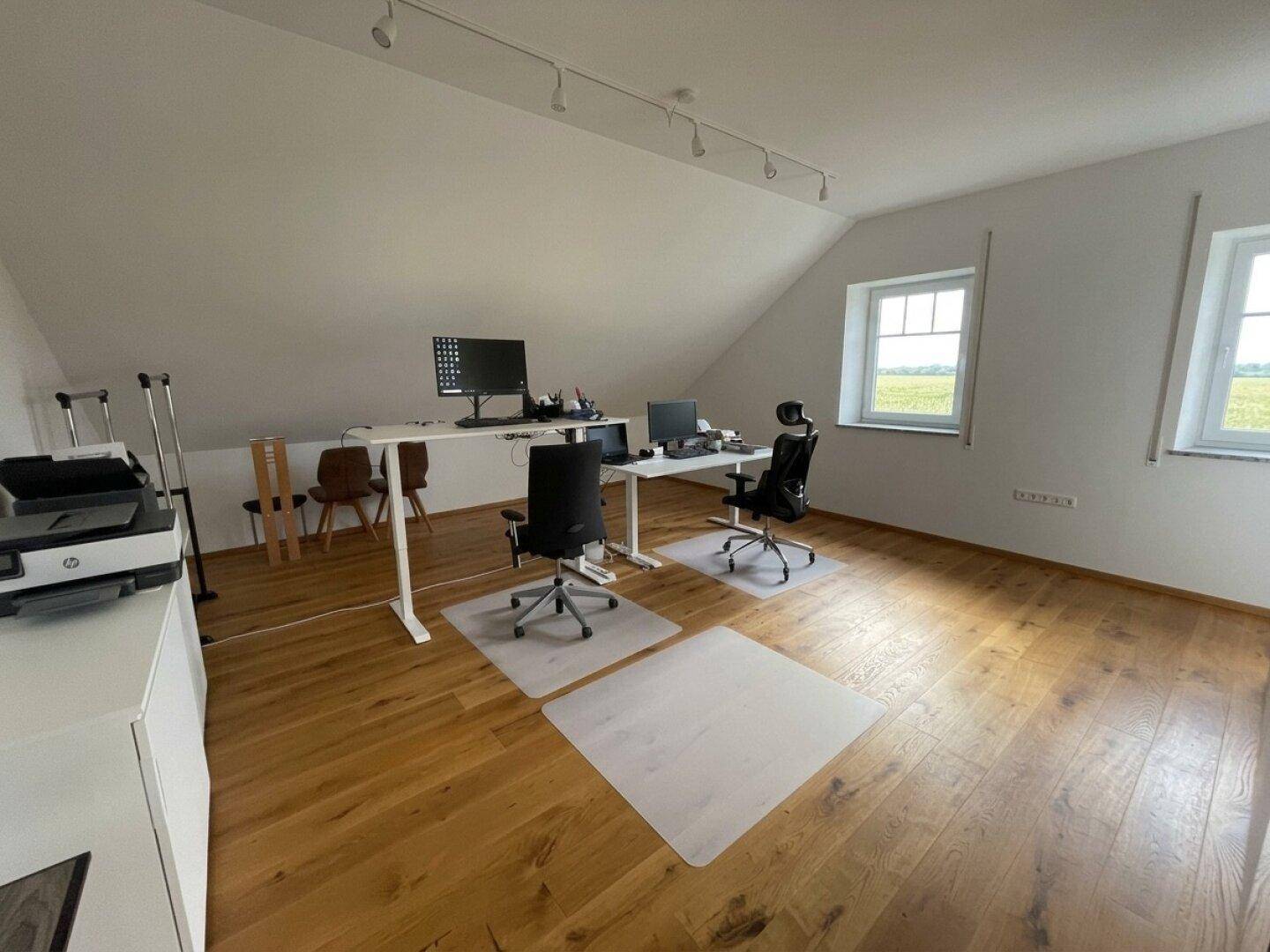 Geräumiges Büro im Dachgeschoss mit Holzboden, zwei Fenstern und viel Tageslicht.