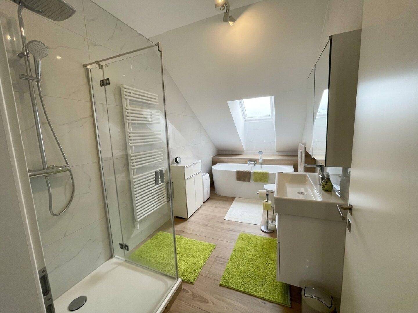 Modernes Badezimmer im Dachgeschoss mit Dusche, Badewanne und Dachfenster.