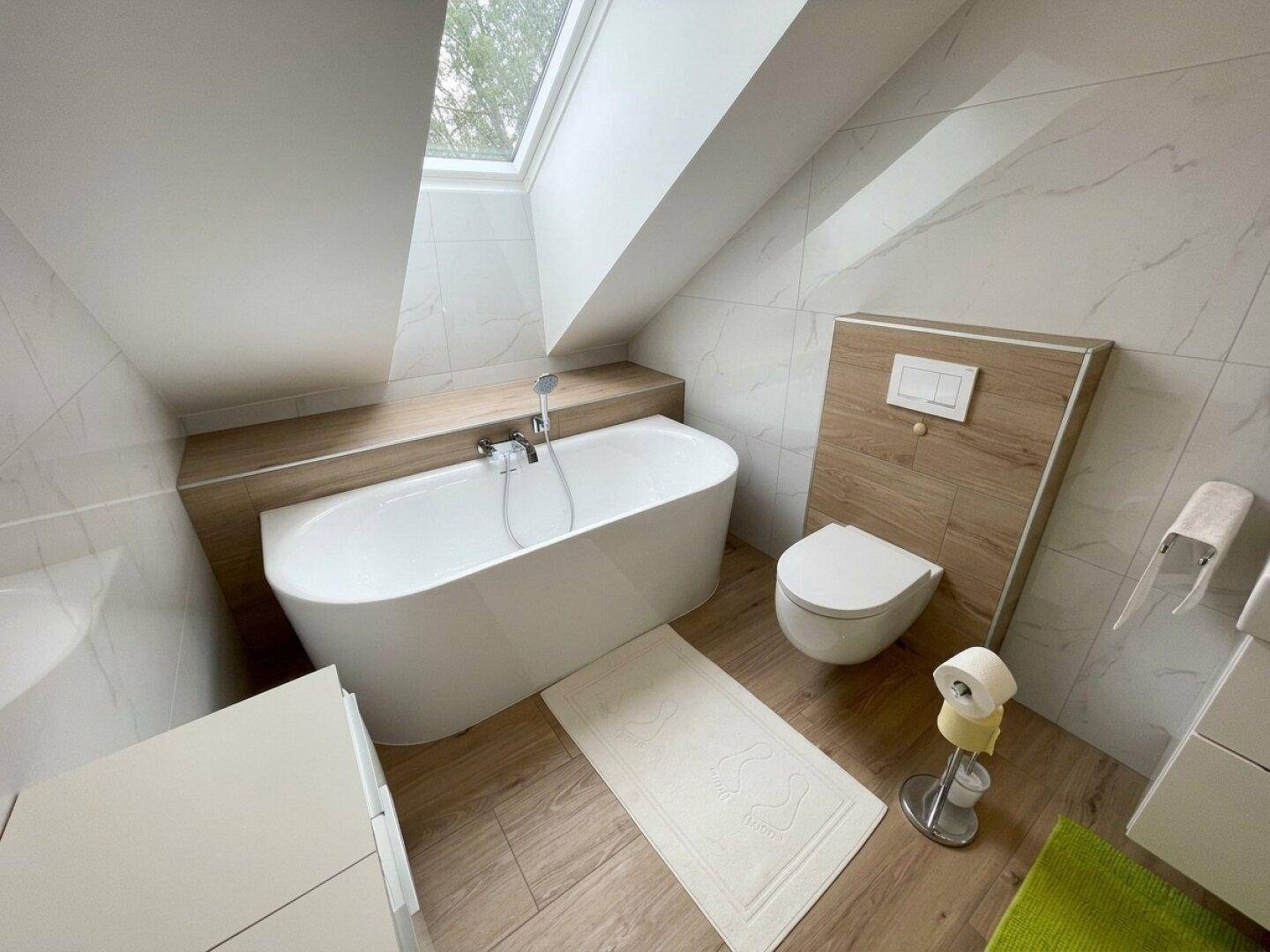 Elegantes Badezimmer mit freistehender Badewanne, Wand-WC und Dachfenster.