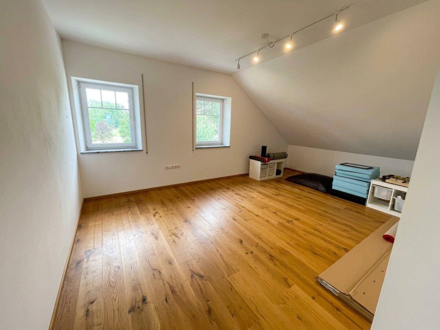 Helles Zimmer im Dachgeschoss mit Holzboden und zwei Fenstern.