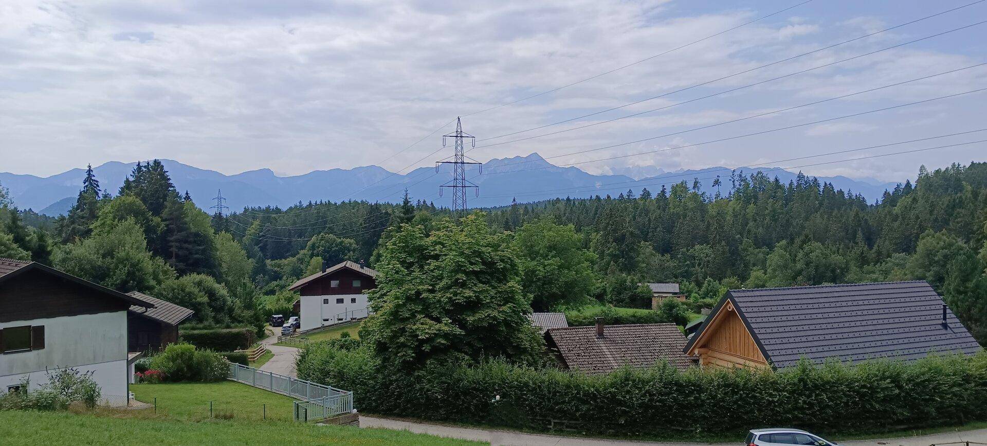 Panoramablick auf eine ländliche Wohngegend mit Bergen im Hintergrund und viel Grün.