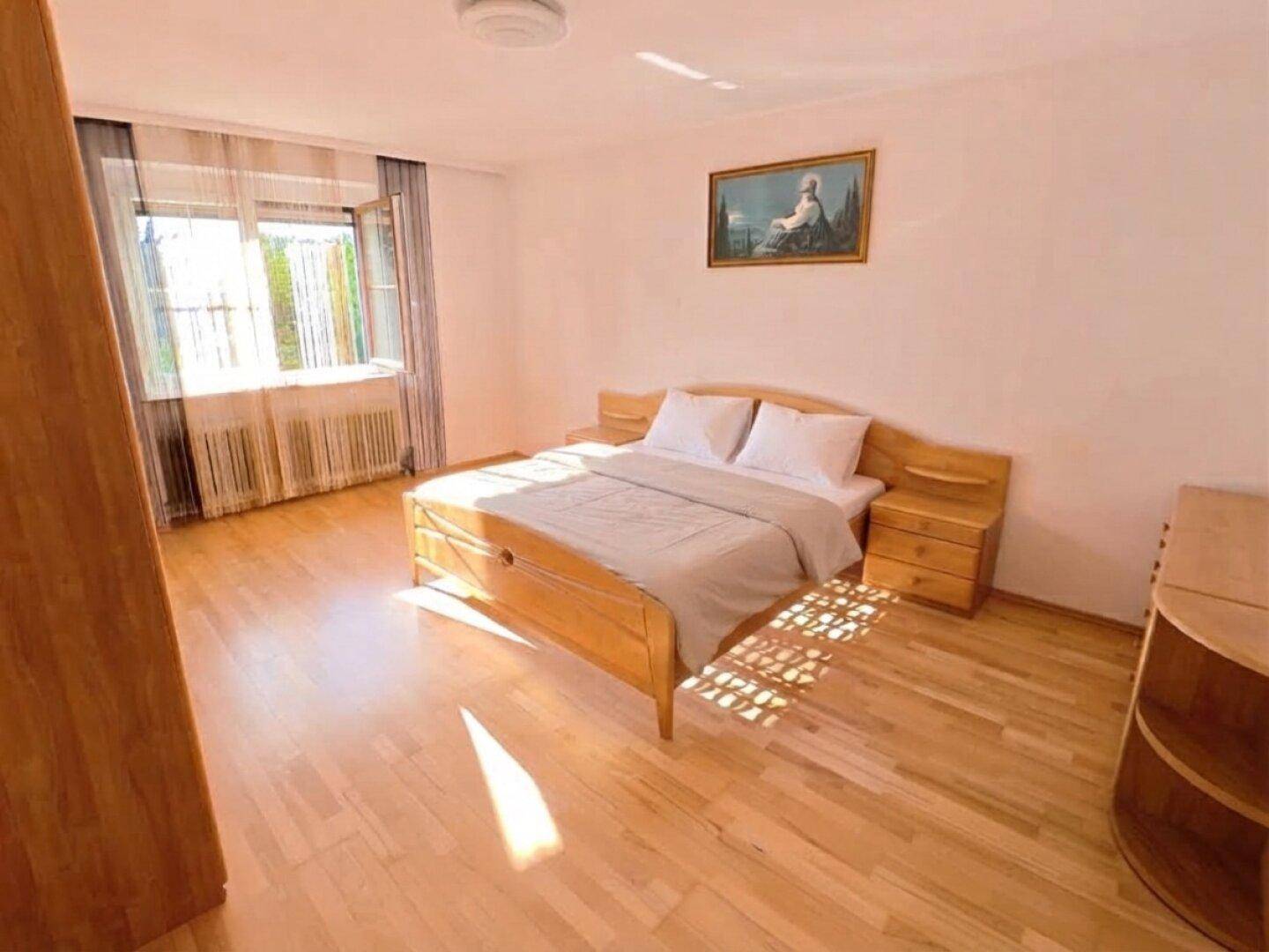 Helles Schlafzimmer mit Doppelbett, Nachttischen und Holzboden, durchflutet von natürlichem Sonnenlicht.