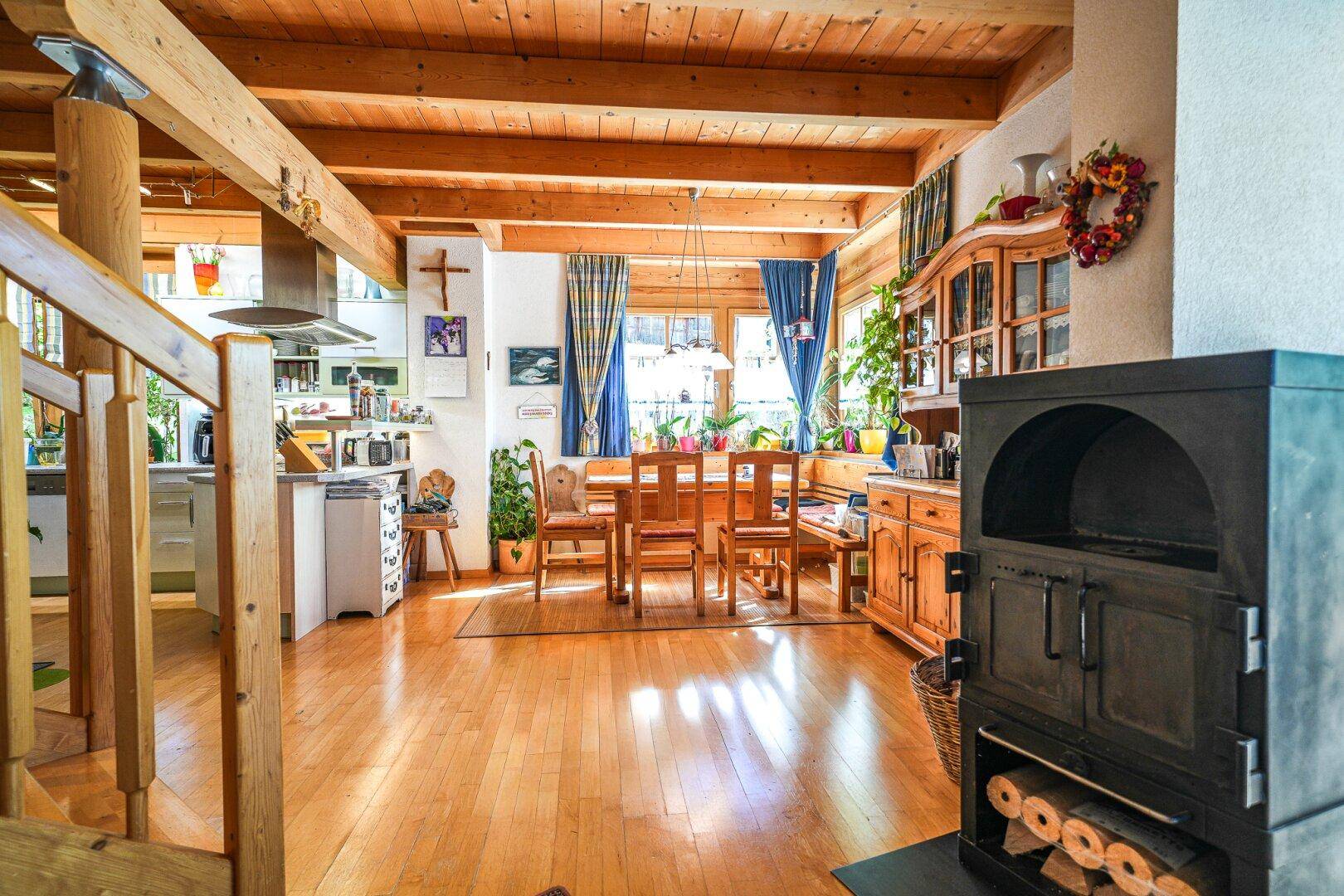 Offener Wohn- und Essbereich mit Holzbalkendecke, Parkettboden und traditionellem Kaminofen.