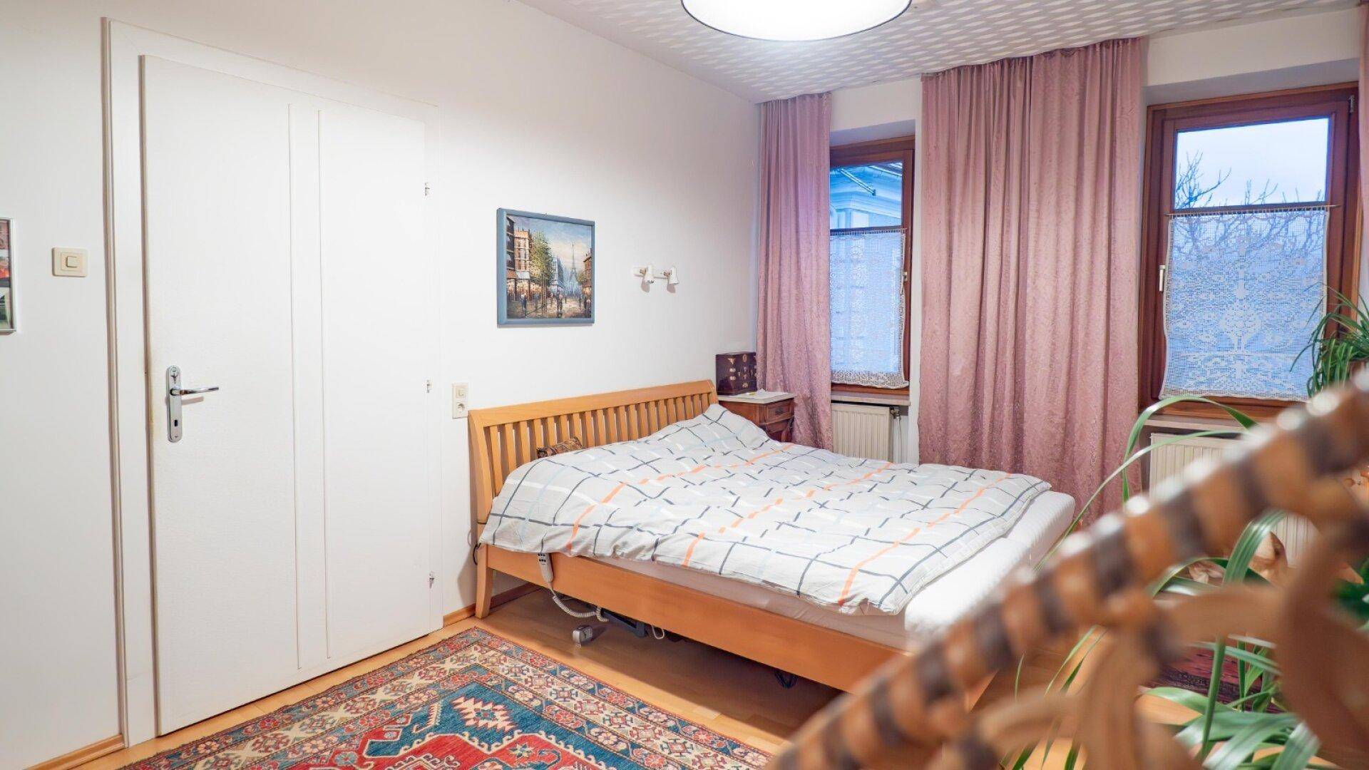 Schlafzimmer mit Holzbett, rosa Vorhängen und Teppichboden in traditionellem Stil.