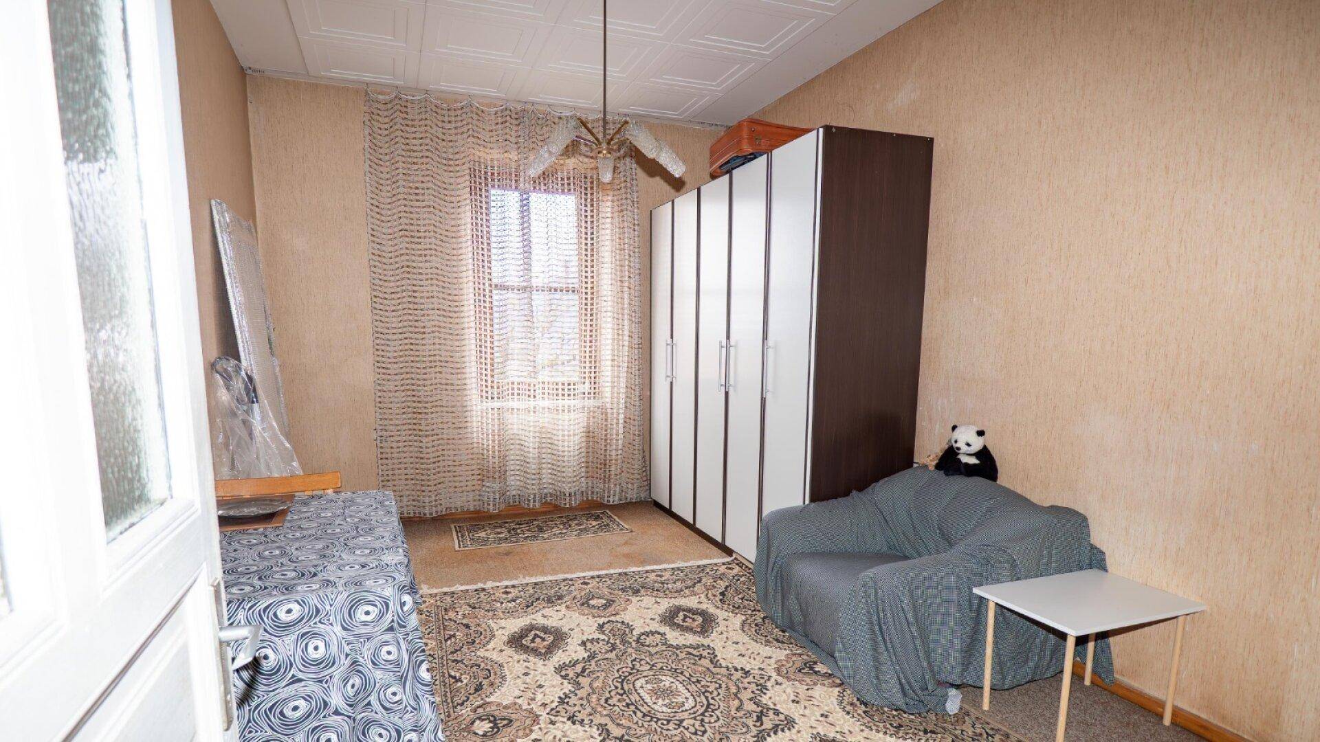 Einfaches Schlafzimmer mit Teppichboden, Kleiderschrank und einem Fenster mit Vorhang.