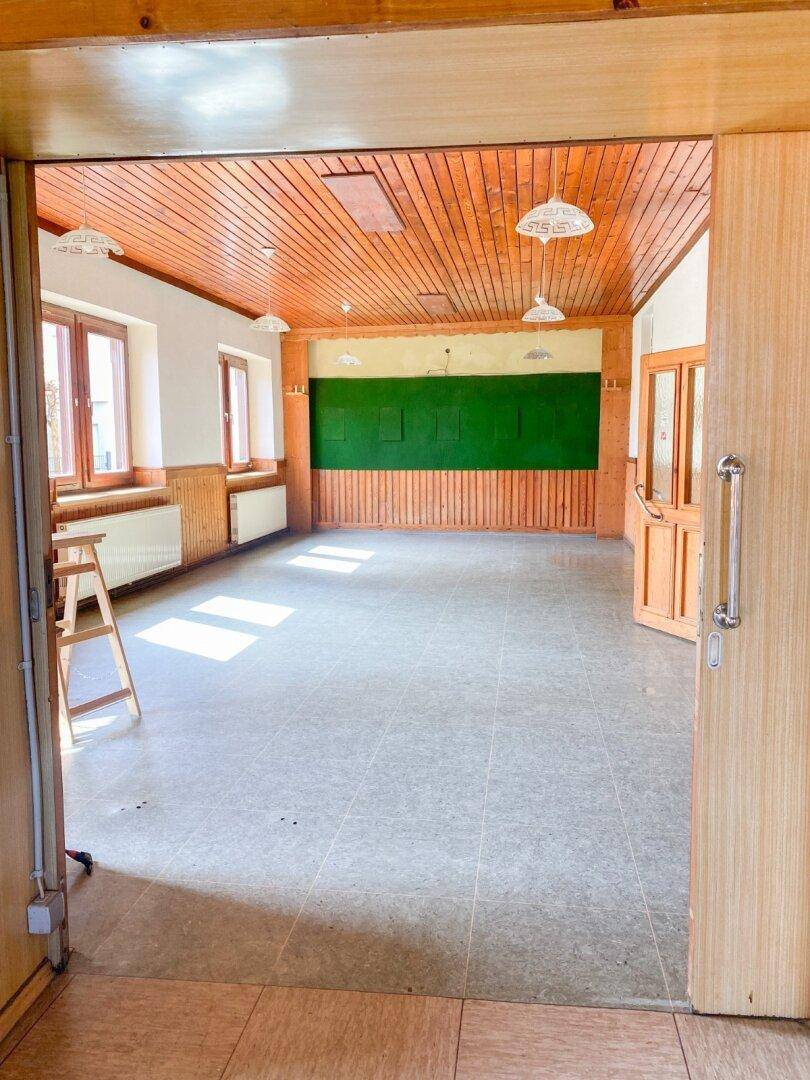 Großer leerer Raum mit Holzdecke, Fliesenboden und grüner Wandtafel.