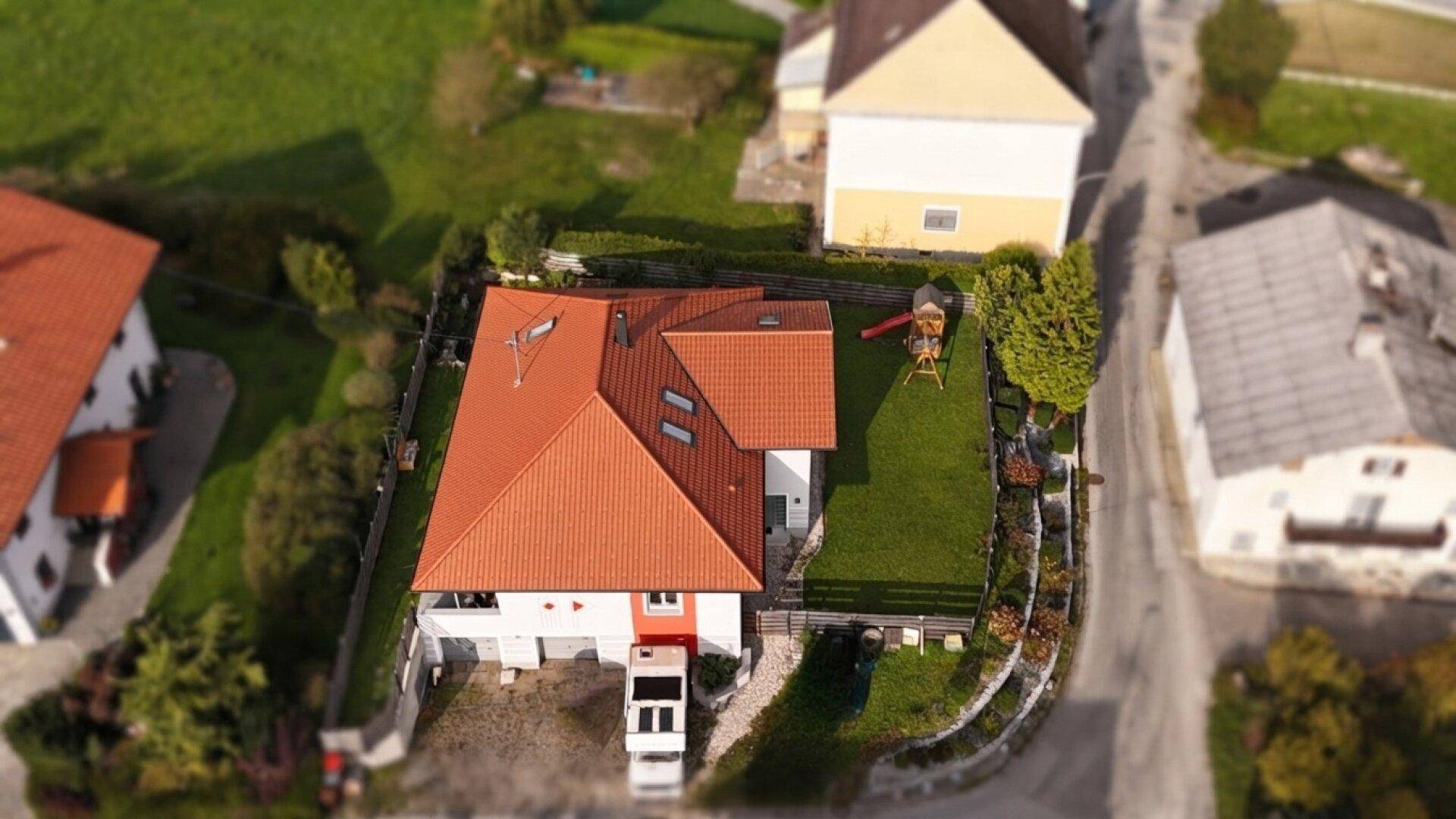 Vogelperspektive des Einfamilienhauses mit rotem Dach, Vorgarten und Zufahrt.