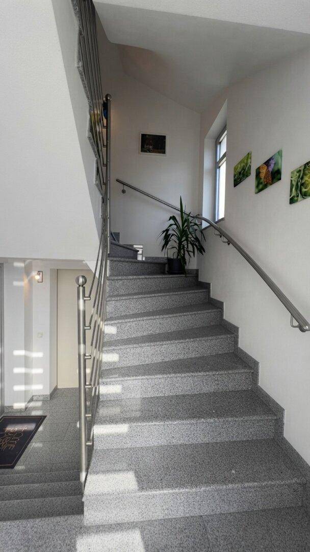 Heller Treppenaufgang mit Granitstufen und modernem Edelstahlgeländer.
