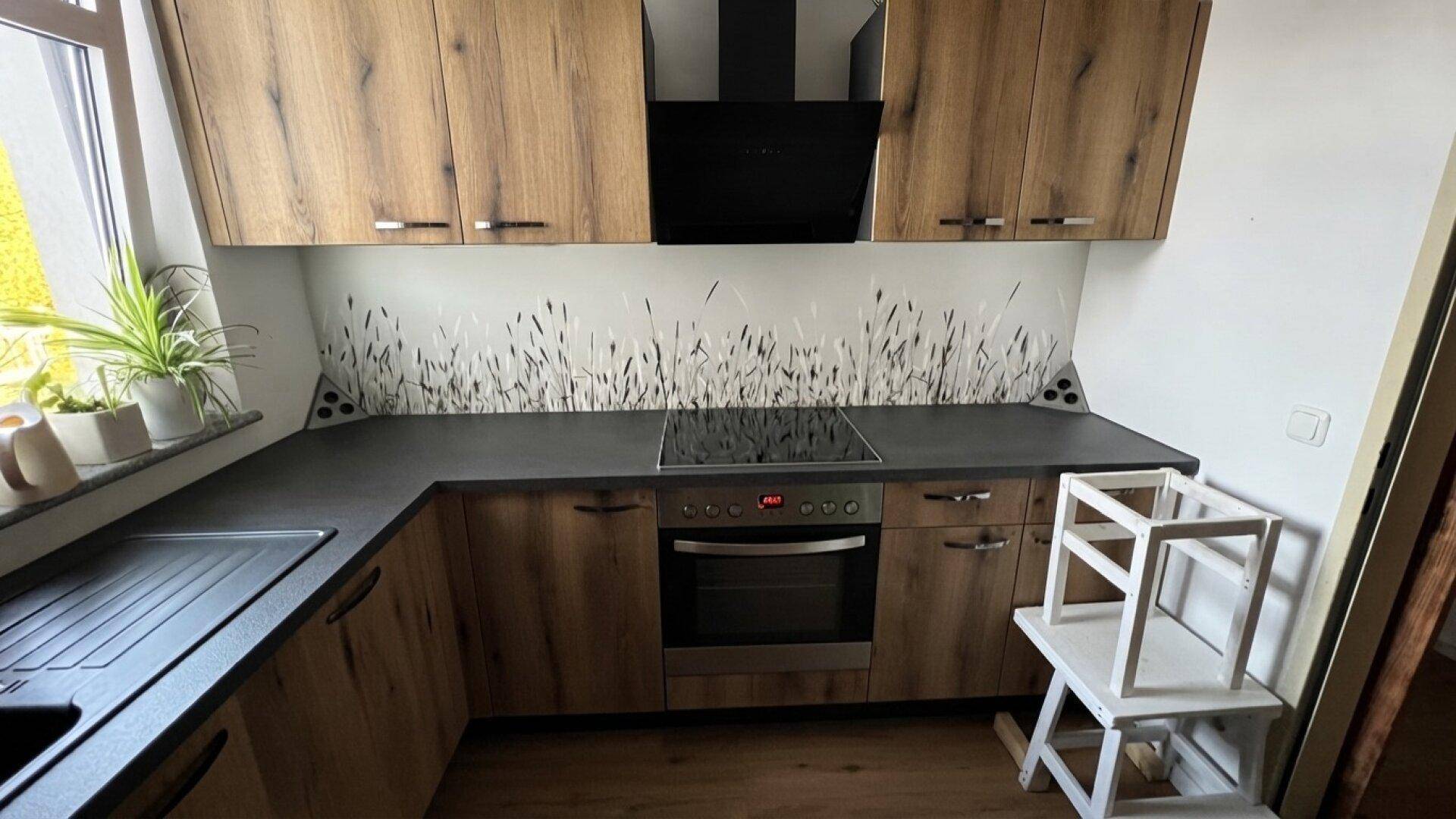 Moderne Einbauküche mit Holzfronten, dunkler Arbeitsplatte und Induktionskochfeld.