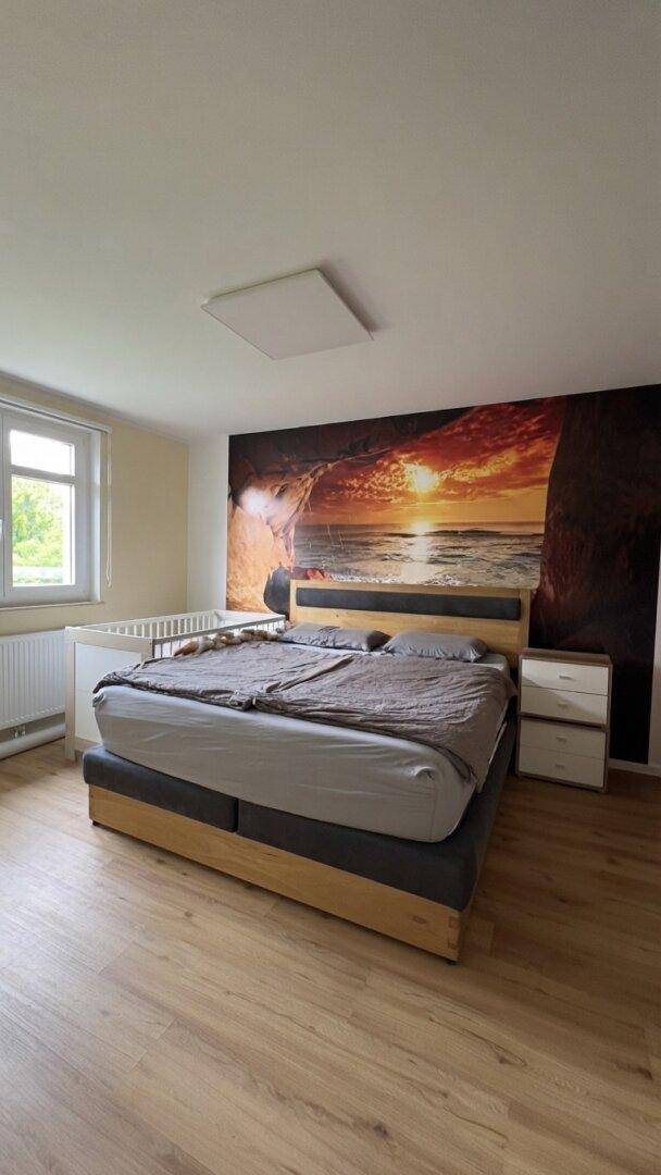 Schlafzimmer mit Doppelbett, Holzboden und großer Wandtapete mit Sonnenuntergangsmotiv.